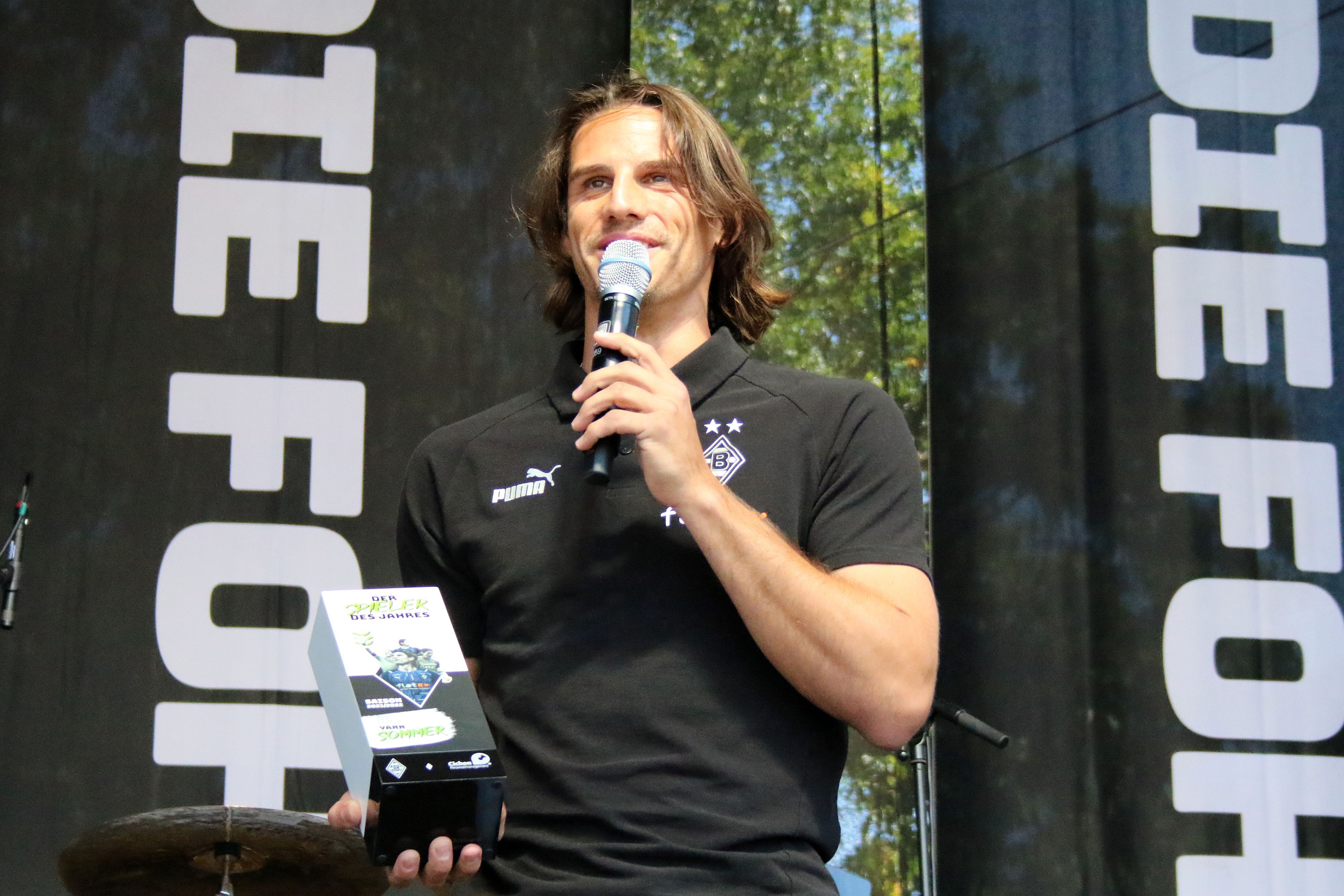 Torhüter Yann Sommer spricht bei der Saisoneröffnung von Borussia Mönchengladbach am 24. Juli 2022 über seine Auszeichnung zum Spieler des Jahres. Sommer hält ein Mikrofon und steht auf einer Bühne, in seiner rechten Hand befindet sich die Trophäe.