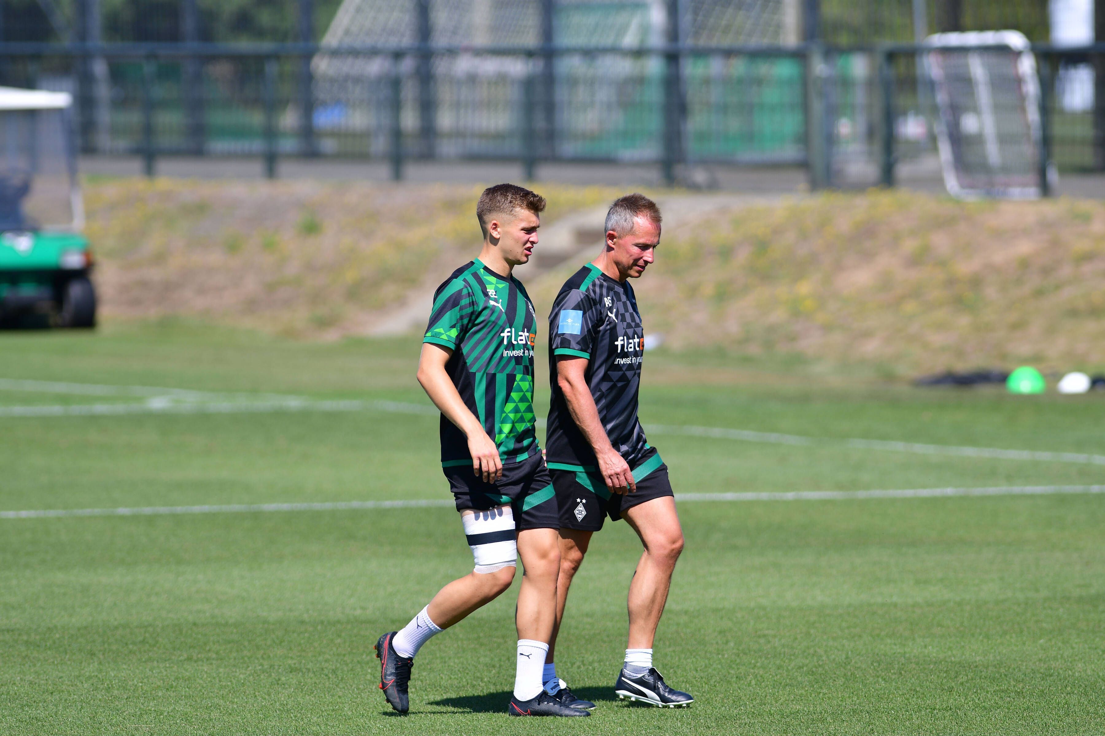 Gladbach-Einkauf Oscar Fraulo (l.) hat am Mittwoch (10. August 2022) das Team-Training wegen einer Blessur abbrechen müssen. Auf diesem Foto ist der Däne zu sehen, wie er mit bandagiertem Oberschenkel, in Begleitung von Physiotherapeut Adam Szordykowski (r.), den Platz verlässt. Fraulo hat das rechte Bein umwickelt.