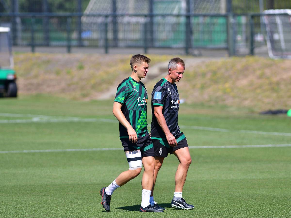 Gladbach-Einkauf Oscar Fraulo (l.) hat am Mittwoch (10. August 2022) das Team-Training wegen einer Blessur abbrechen müssen. Auf diesem Foto ist der Däne zu sehen, wie er mit bandagiertem Oberschenkel, in Begleitung von Physiotherapeut Adam Szordykowski (r.), den Platz verlässt. Fraulo hat das rechte Bein umwickelt.