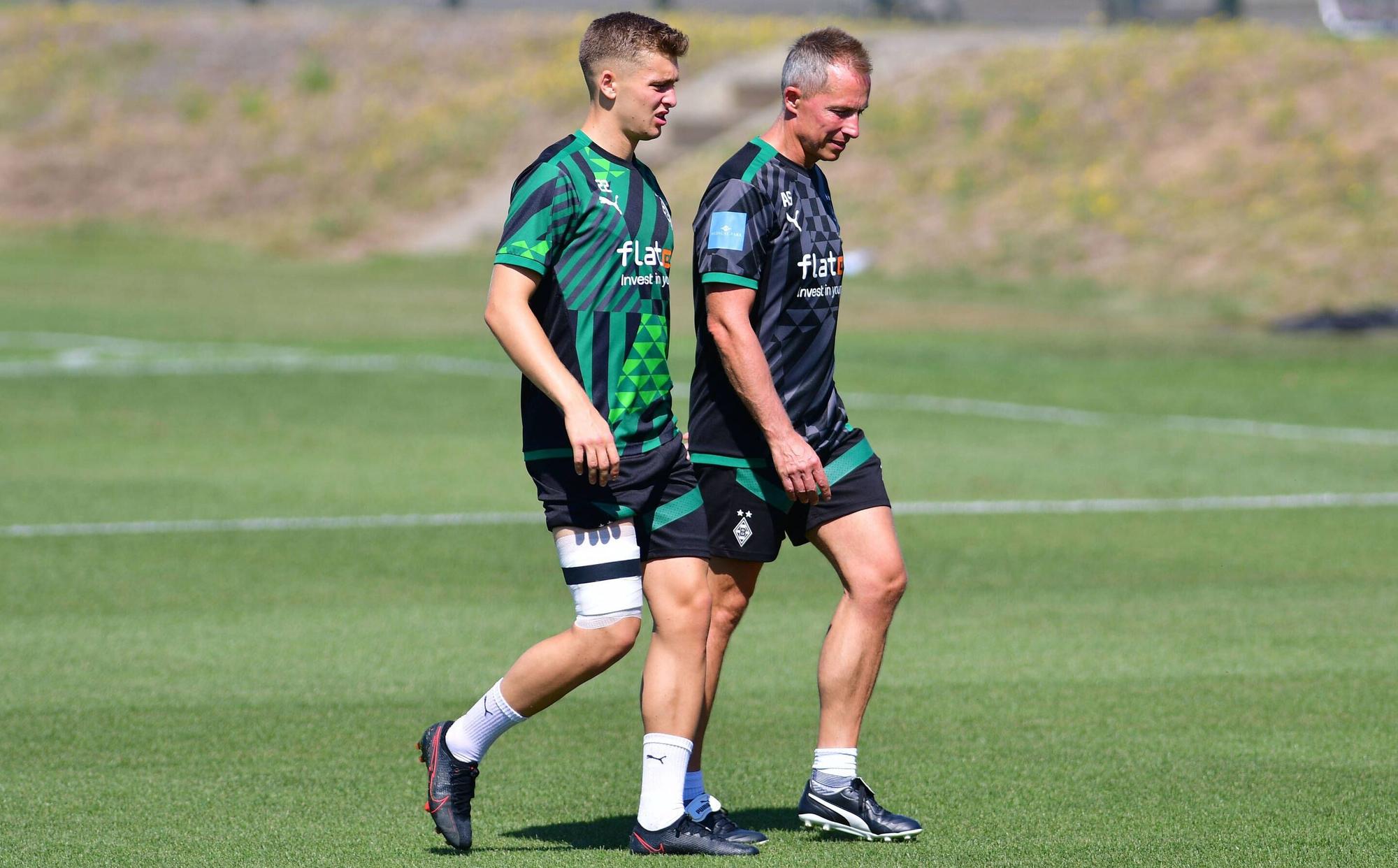 Gladbach-Einkauf Oscar Fraulo (l.) hat am Mittwoch (10. August 2022) das Team-Training wegen einer Blessur abbrechen müssen. Auf diesem Foto ist der Däne zu sehen, wie er mit bandagiertem Oberschenkel, in Begleitung von Physiotherapeut Adam Szordykowski (r.), den Platz verlässt. Fraulo hat das rechte Bein umwickelt.