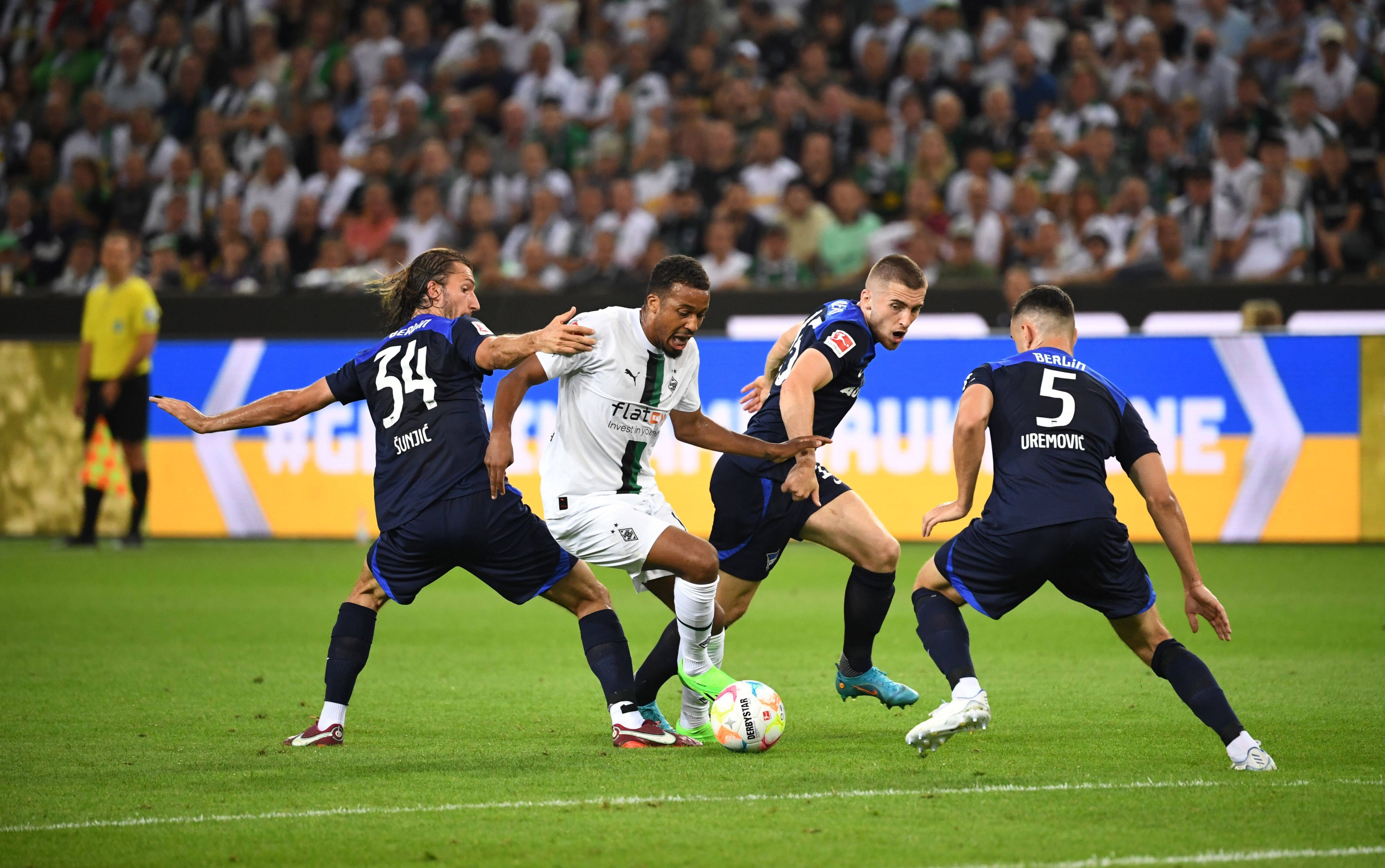 Gladbachs Alassane Plea (weiß, Mitte) im Zweikampf mit Berlins Ivan Sunjic (Nr. 34), Jonjoe Kenny (blau, Mitte) und Filip Uremovic (Nr. 5). Plea erzielte am 19. August 2022 die 1:0-Führung für Borussia Mönchengladbach gegen Hertha BSC per Elfmeter.