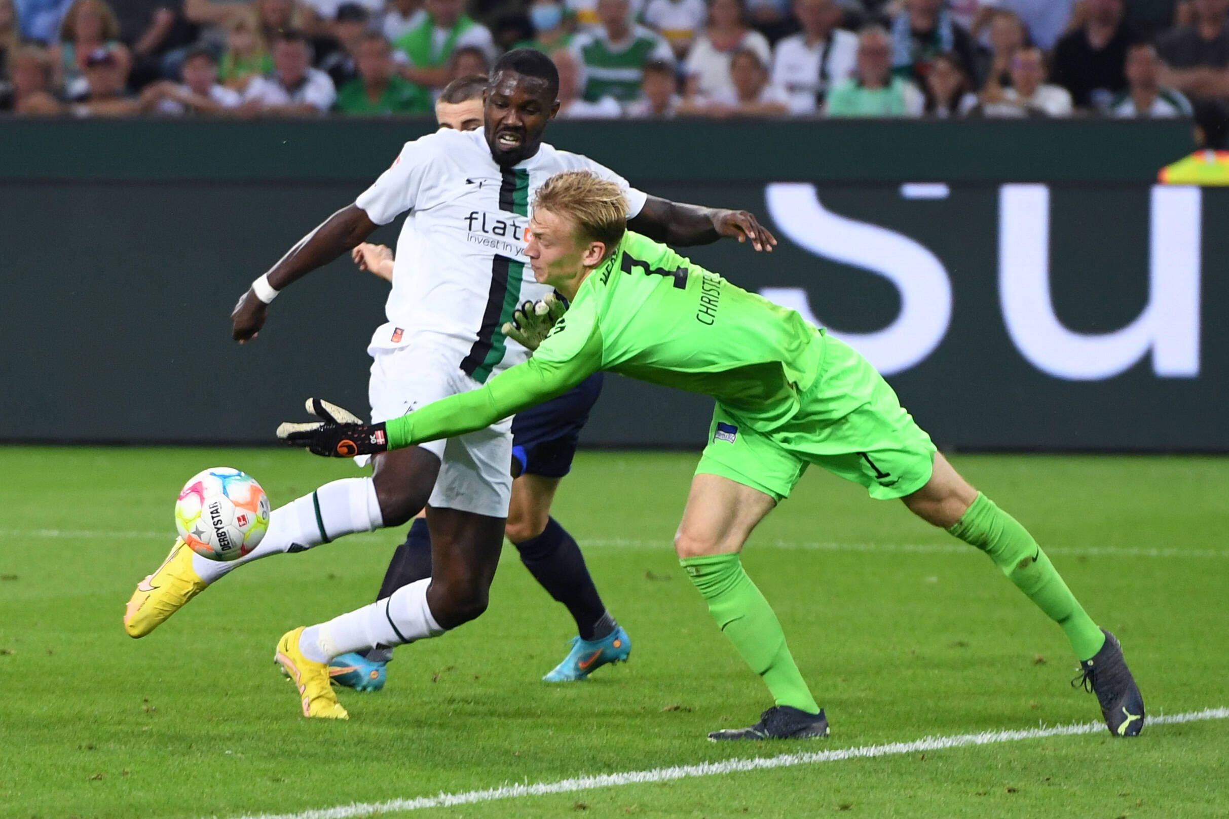 Gladbach-Stürmer Marcus Thuram (l.) im Duell mit Hertha-Schlussmann Oliver Christensen (r.) während der Bundesliga-Partie am Freitag (19. August 2022) im Borussia-Park. Beide schauen auf den Ball.