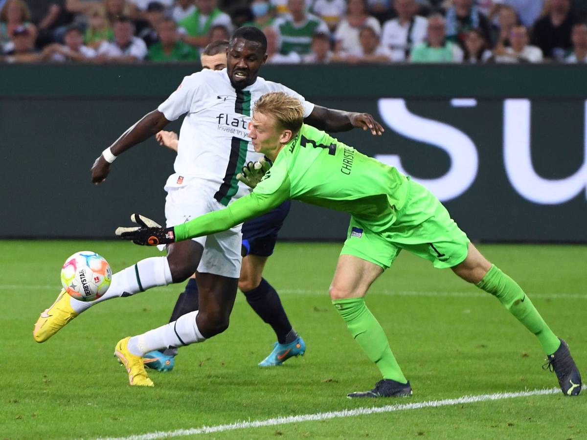 Gladbach-Stürmer Marcus Thuram (l.) im Duell mit Hertha-Schlussmann Oliver Christensen (r.) während der Bundesliga-Partie am Freitag (19. August 2022) im Borussia-Park. Beide schauen auf den Ball.