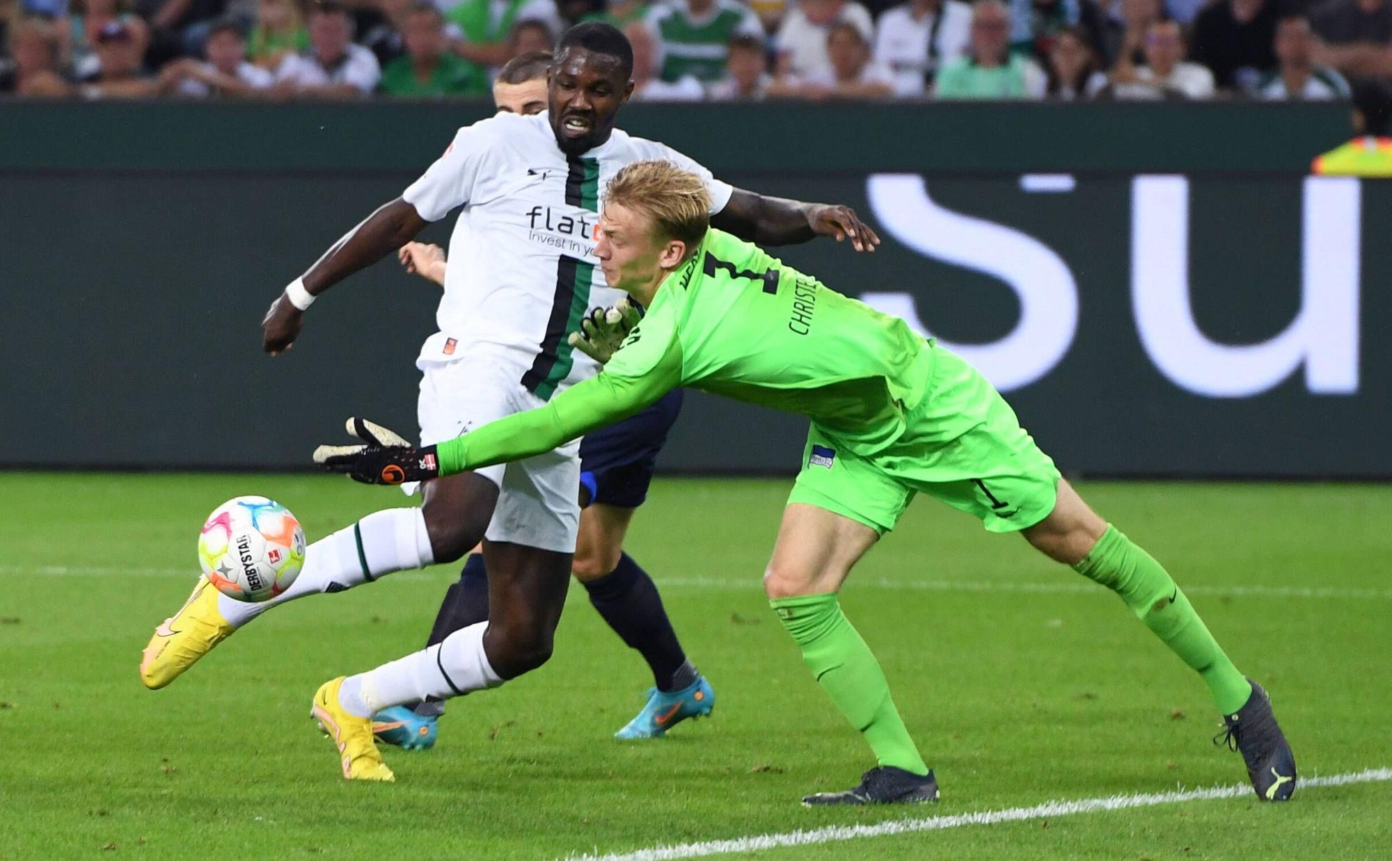 Gladbach-Stürmer Marcus Thuram (l.) im Duell mit Hertha-Schlussmann Oliver Christensen (r.) während der Bundesliga-Partie am Freitag (19. August 2022) im Borussia-Park. Beide schauen auf den Ball.