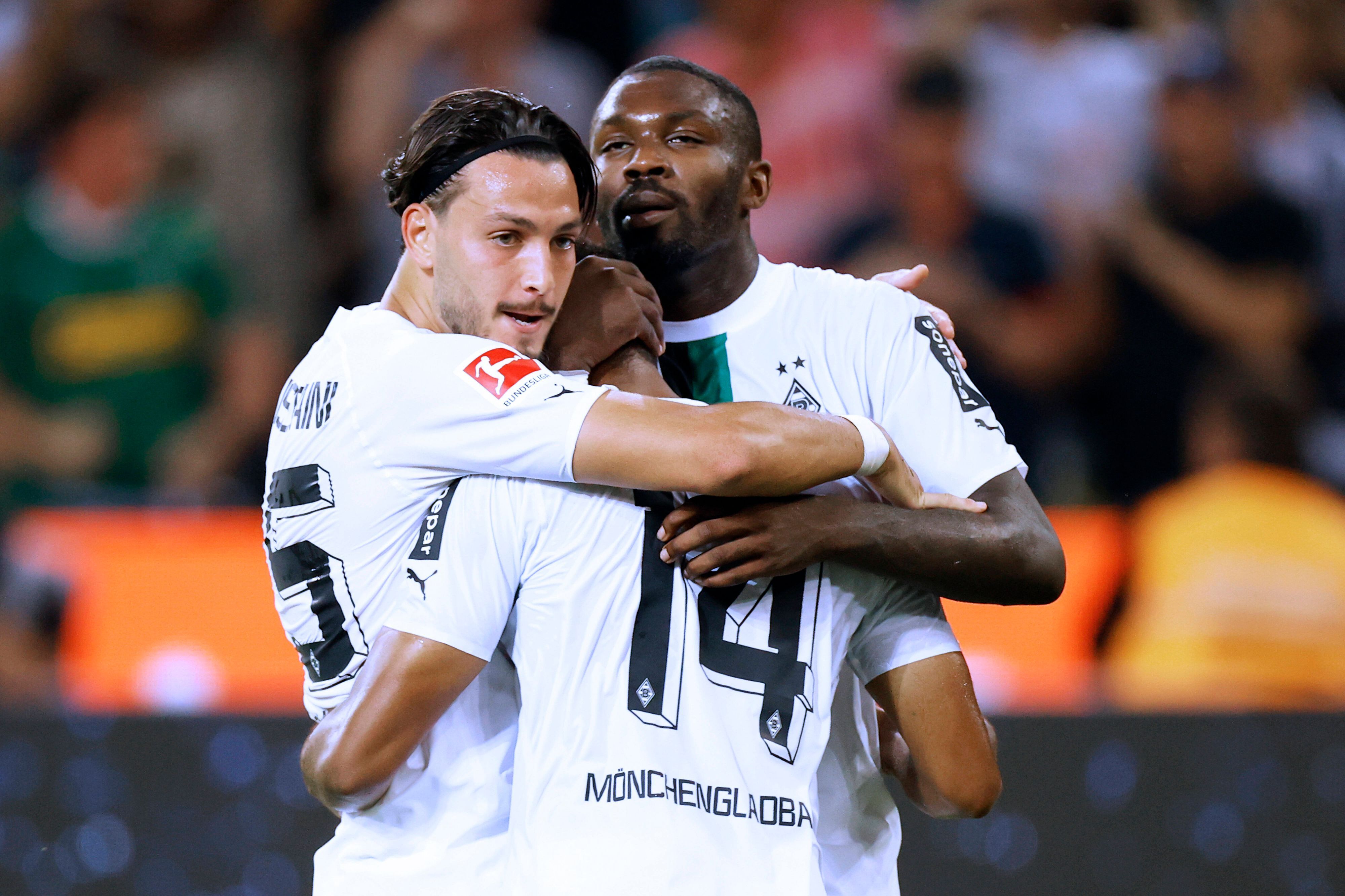 Die Gladbach-Profis Ramy Bensebaini (l.) und Marcus Thuram (r.) umarmen ihren Teamkollegen Alassane Plea, hier zu sehen am 19. August 2022 im Borussia-Park. Von Plea ist die Rückseite zu sehen.