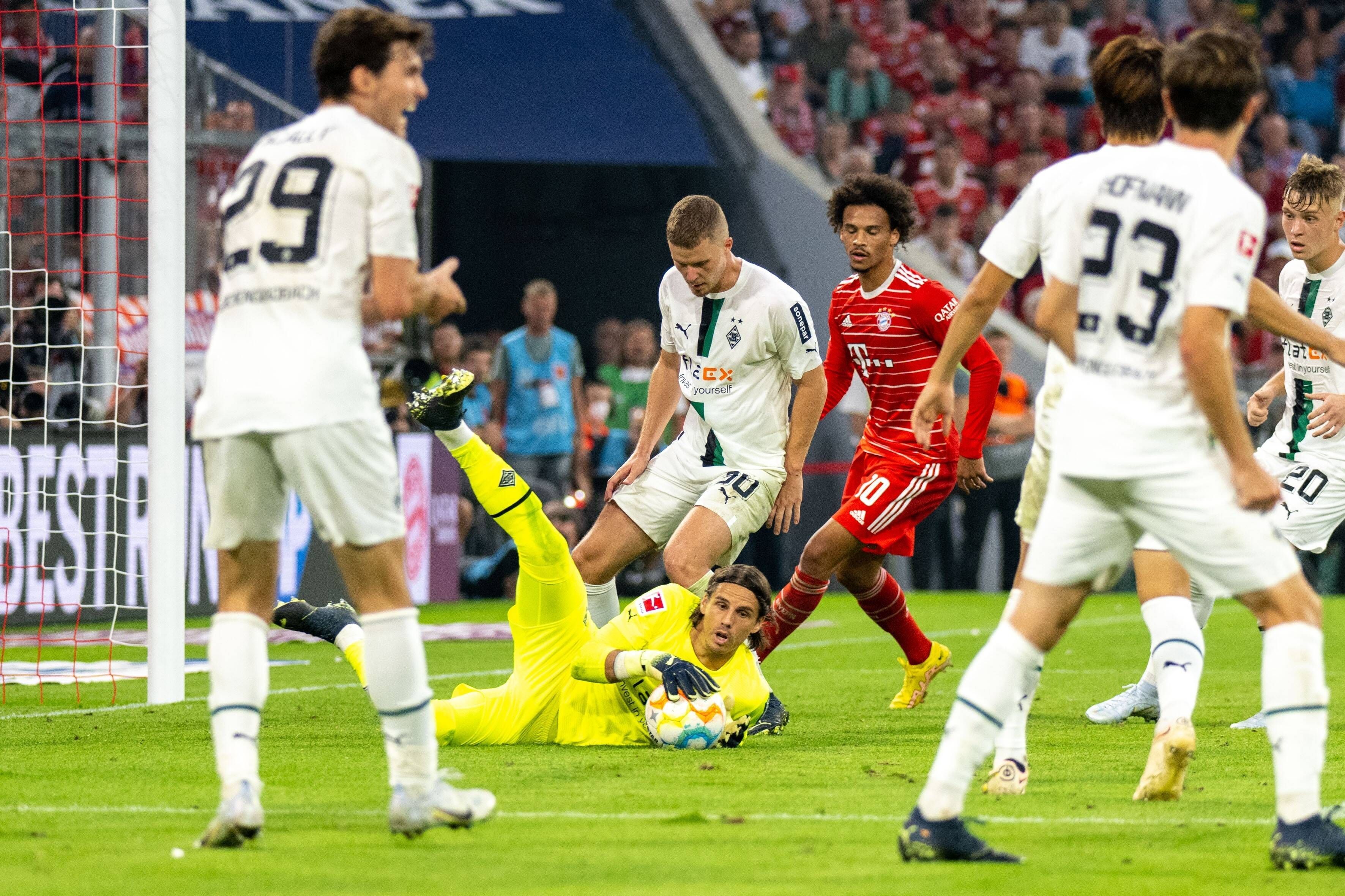 Yann Sommer, Torwart Borussia Mönchengladbach, liegt, umgeben von Spielern, auf dem Spielfeld und hält den Ball fest. Dieses Foto zeigt den Schweizer Nationalspieler am 27. August 2022 in der Allianz-Arena gegen Bayern München. Sommer trägt ein gelbes Trikot und schaut aufmerksam zur Seite.