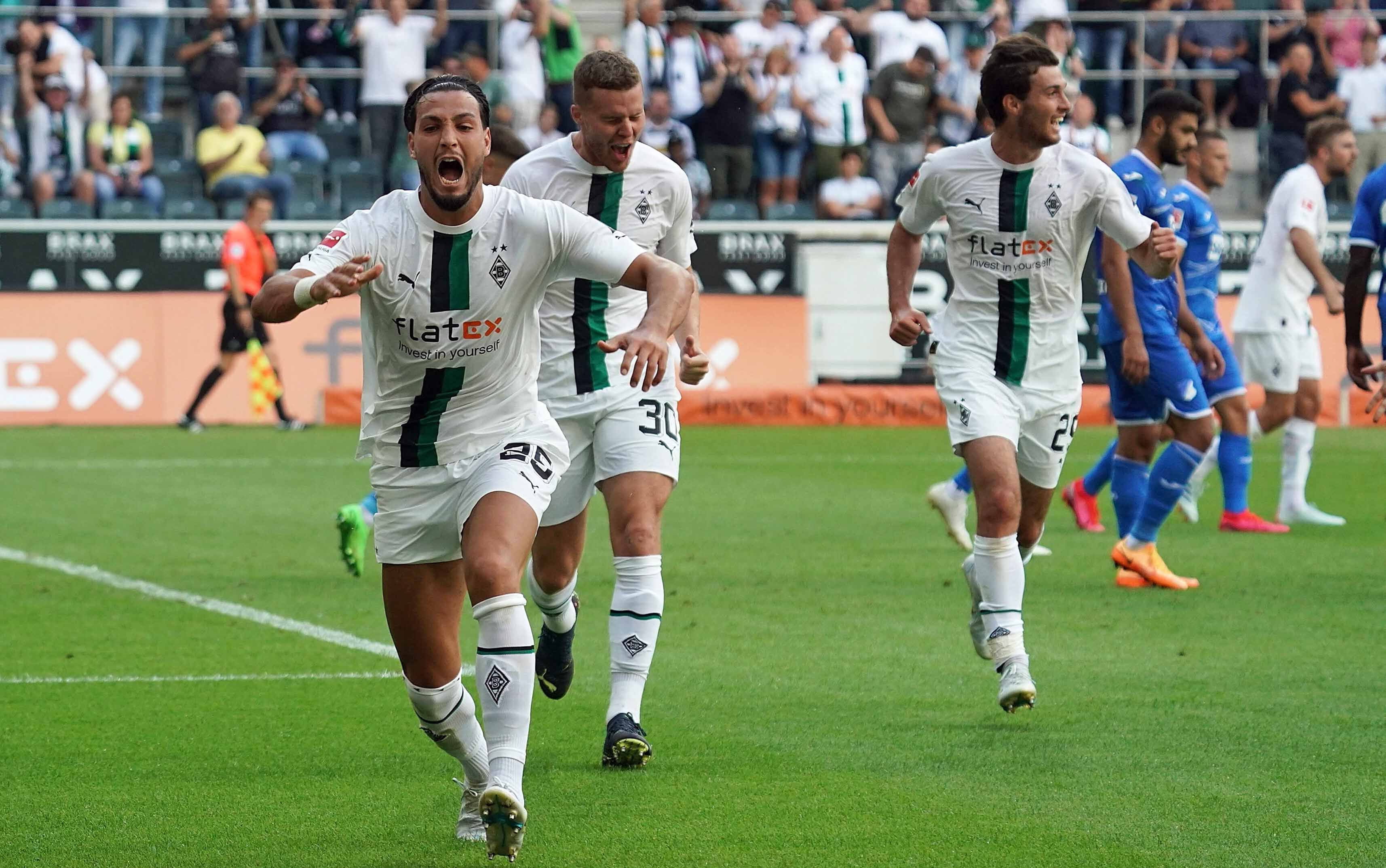 Gladbach-Profi Ramy Bensebaini (l.) bejubelt seinen Fallrückzieher-Treffer im Bundesliga-Duell gegen die TSG Hoffenheim am 6. August 2022 im Borussia-Park. Im Hintergrund sind seine Team-Kollegen Nico Elvedi und Joe Scally zu sehen.
