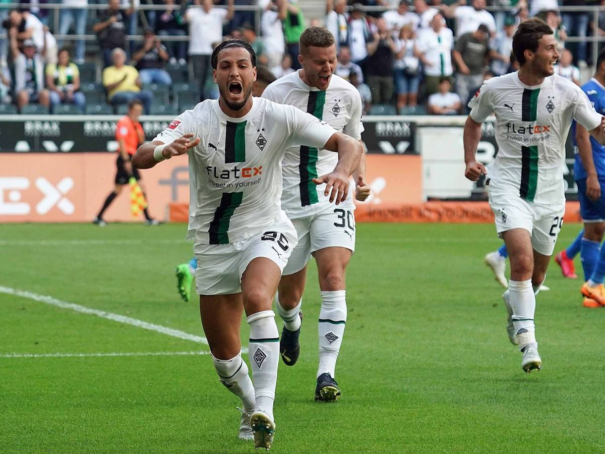 Gladbach-Profi Ramy Bensebaini (l.) bejubelt seinen Fallrückzieher-Treffer im Bundesliga-Duell gegen die TSG Hoffenheim am 6. August 2022 im Borussia-Park. Im Hintergrund sind seine Team-Kollegen Nico Elvedi und Joe Scally zu sehen.