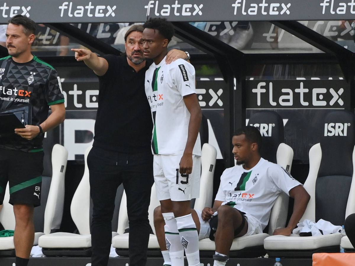 Trainer Daniel Farke von Borussia Mönchengladbach gibt Nathan Ngoumou Anweisung vor dessen Einwechslung am 4. September 2022 gegen Mainz 05. Farke hat den Arm um Ngoumous Schulter gelegt und zeigt mit dem anderen Arm auf das Spielfeld. Links steht Co-Trainer Edmund Riemer, im Hintergrund sitzt Alassane Plea auf der Bank.