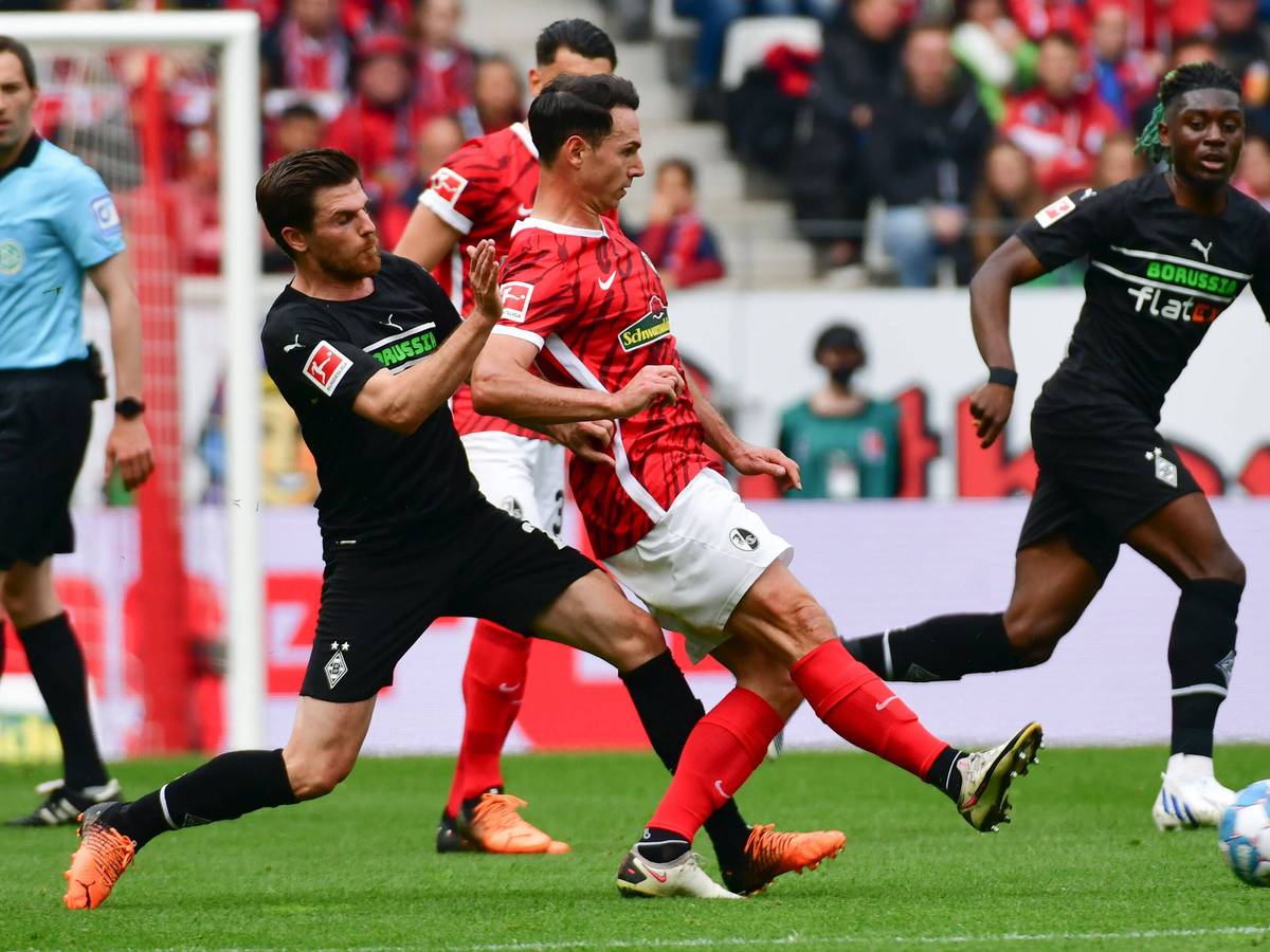 Jonas Hofmann (l.) und Nicolas Höfler (mitte) vom SC Freiburg im Zweikampf im letzten Aufeinandertreffen am 23. April 2022. Höfler spielt den Ball nach rechts während Hofmann ihn mit seinem linken Bein bei der Ballabgabe stört.