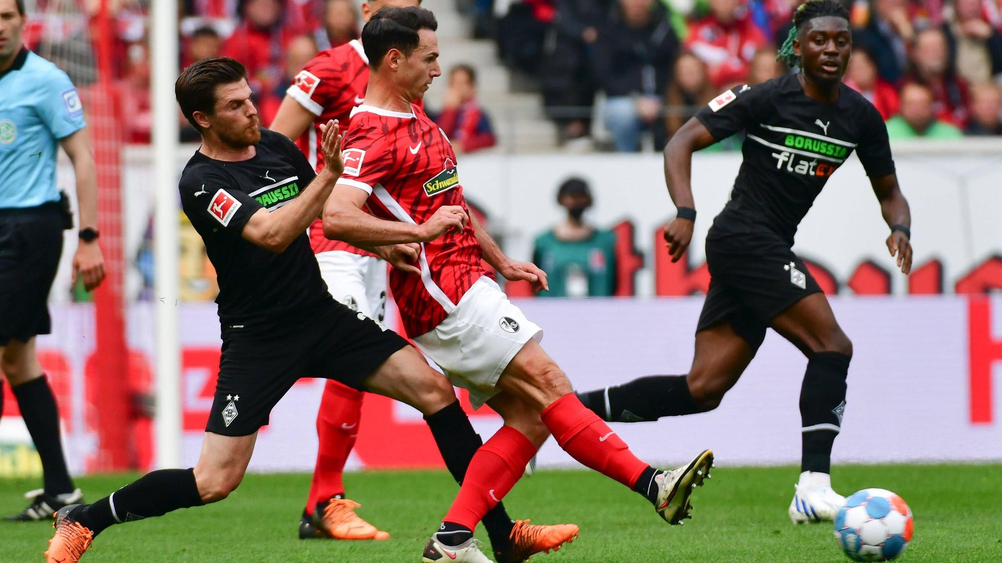 Jonas Hofmann (l.) und Nicolas Höfler (mitte) vom SC Freiburg im Zweikampf im letzten Aufeinandertreffen am 23. April 2022. Höfler spielt den Ball nach rechts während Hofmann ihn mit seinem linken Bein bei der Ballabgabe stört.