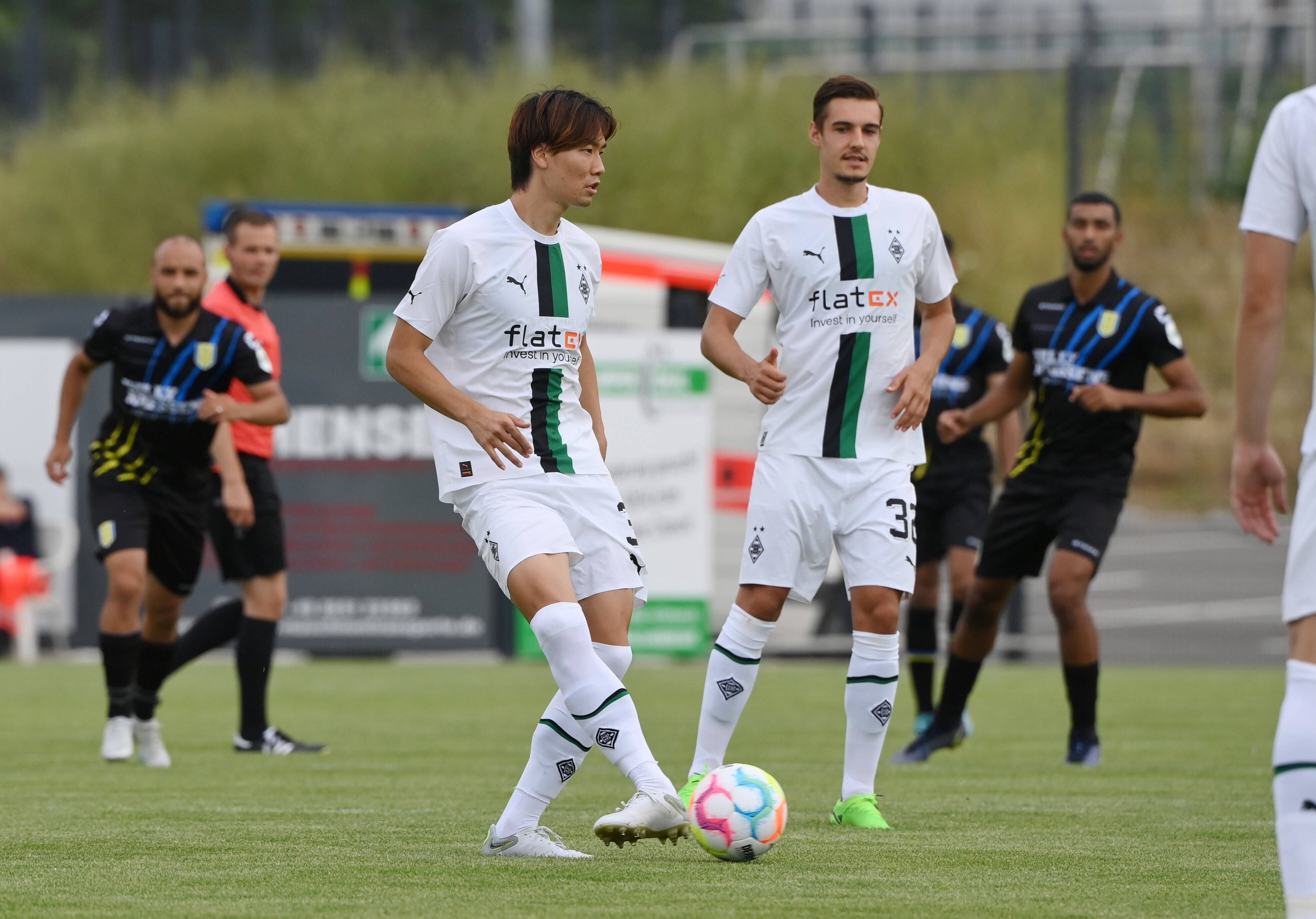 Die Gladbach-Profis Ko Itakura (l.) und Florian Neuhaus (r.) haben sich schwere Knieverletzungen zugezogen. Auf diesem Foto sind die beiden am 20. Juli 2022 bei einem Testspiel in Velbert zu sehen. Itakura hat den Ball am Fuß, Neuhaus schaut zu ihm.
