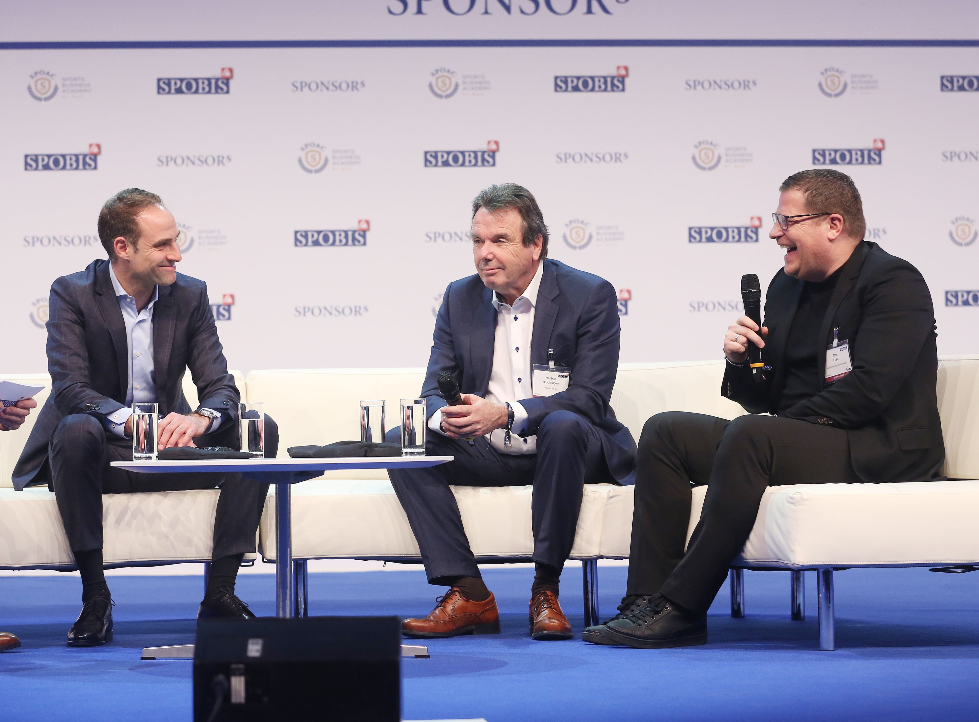 Gute Laune: Geschäftsführer Oliver Mintzlaff von RB Leipzig (l.) mit Heribert Bruchhagen (M.), Ex-Vorstand Hamburger SV, und Ex-Gladbach-Manager Max Eberl (r.) während des Sportbusiness-Kongress „SPOBIS“ am 30. Januar 2018 in Düsseldorf. Eberl hält ein Mikrofon in der Hand.