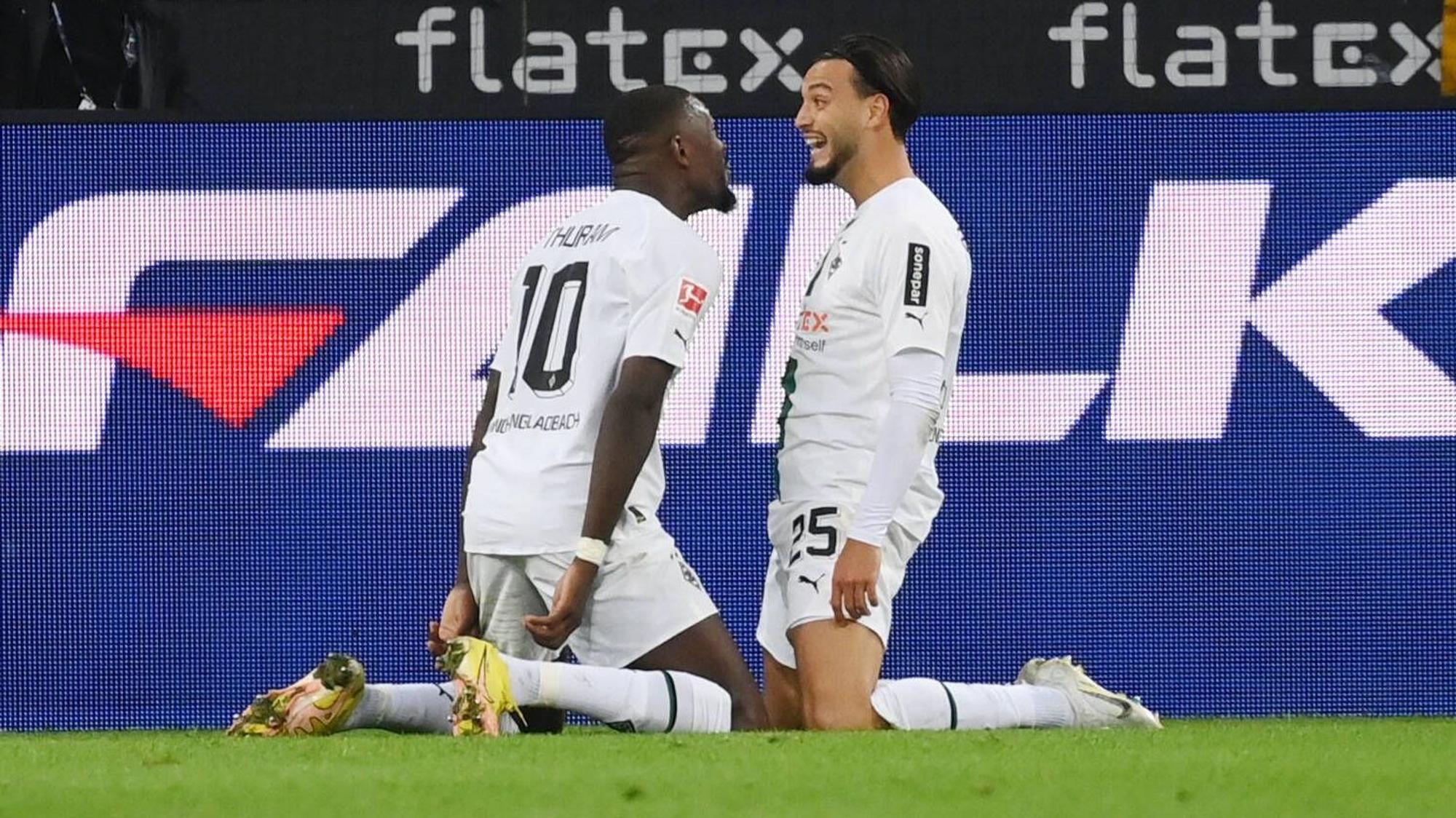 Gladbach-Profi Ramy Bensebaini (l.) jubelt gemeinsam mit Marcus Thuram über seinen Bundesliga-Treffer beim 3:0-Sieg gegen RB Leipzig am 17. September 2022 im Borussia-Park. Beide Spieler knien auf dem Rasen.