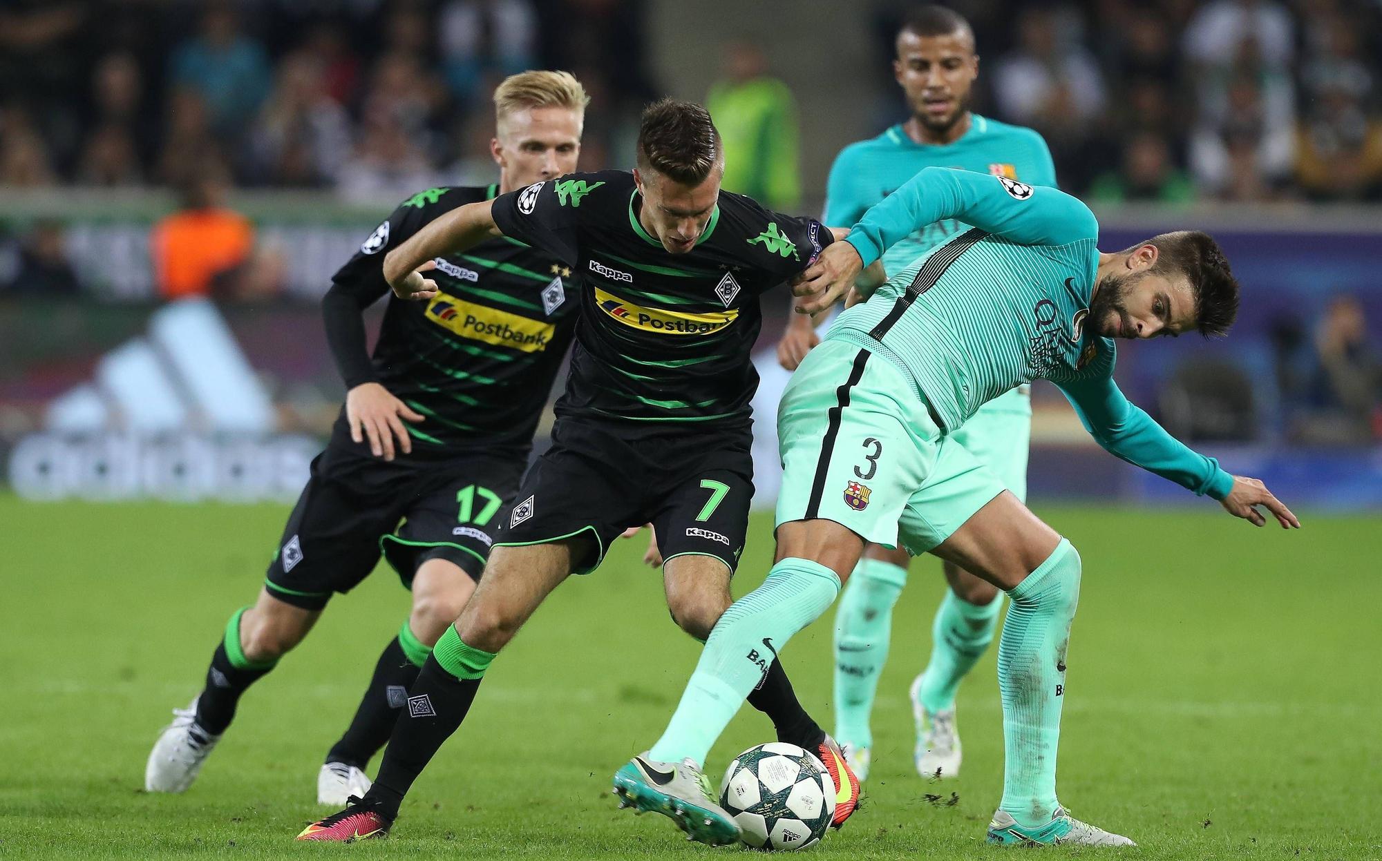 Gladbach-Profi Patrick Herrmann (Mitte) im Champions-League-Duell am 28. September 2016 mit dem FC Barcelona im Borussia-Park. In dieser Szene befindet sich der Flügelflitzer im Zweikampf mit Abwehrspieler Gerard Piqué. Beide Spieler haben jeweils den Ball im Blick.
