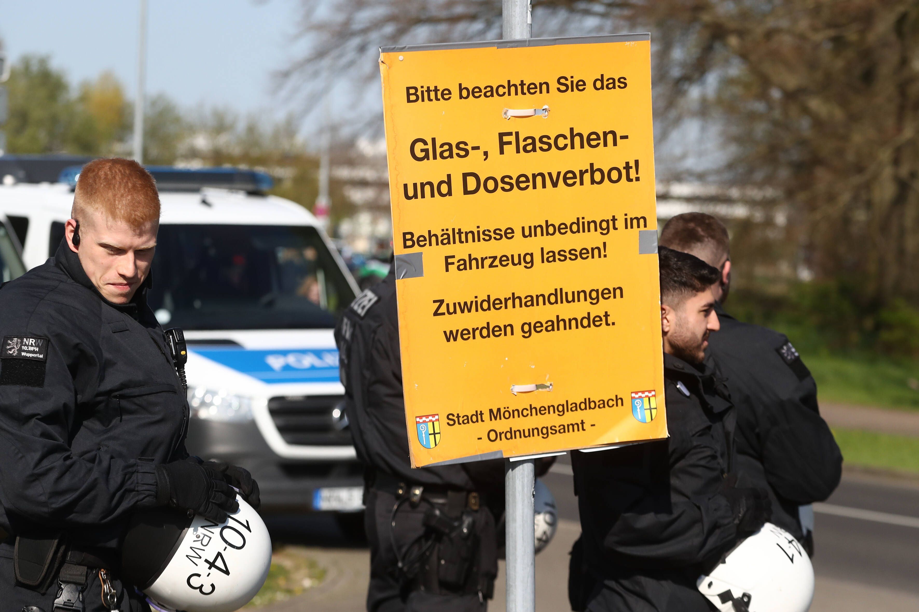 Wie in jedem Jahr wird es rund um das Derby zwischen Borussia Mönchengladbach und dem 1. FC Köln zahlreiche Sicherheitsmaßnahmen geben. Das Foto zeigt Polizeibeamte beim vergangenen Derby am 16. April 2022 mit einem Schild, dass auf das Glas-, Flaschen- und Dosenverbot hinweist.