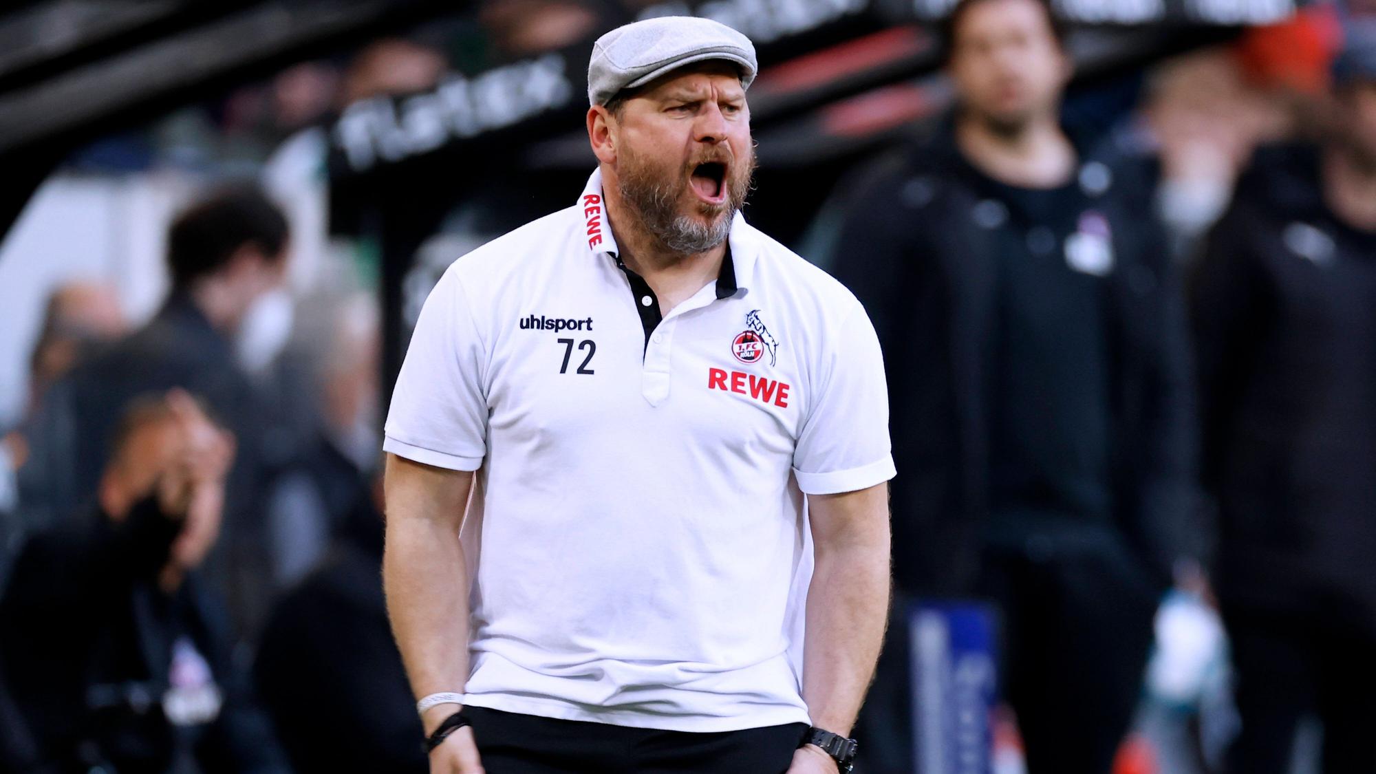 Steffen Baumgart, Trainer des 1. FC Köln, gestikuliert und schreit an der Seitenlinie im Gladbacher Borussia-Park. Dieses Foto stammt vom 16. April 2022. Baumgart trägt eine Jogginghose und ein weißes Polohemd, dazu eine Schiebermütze.