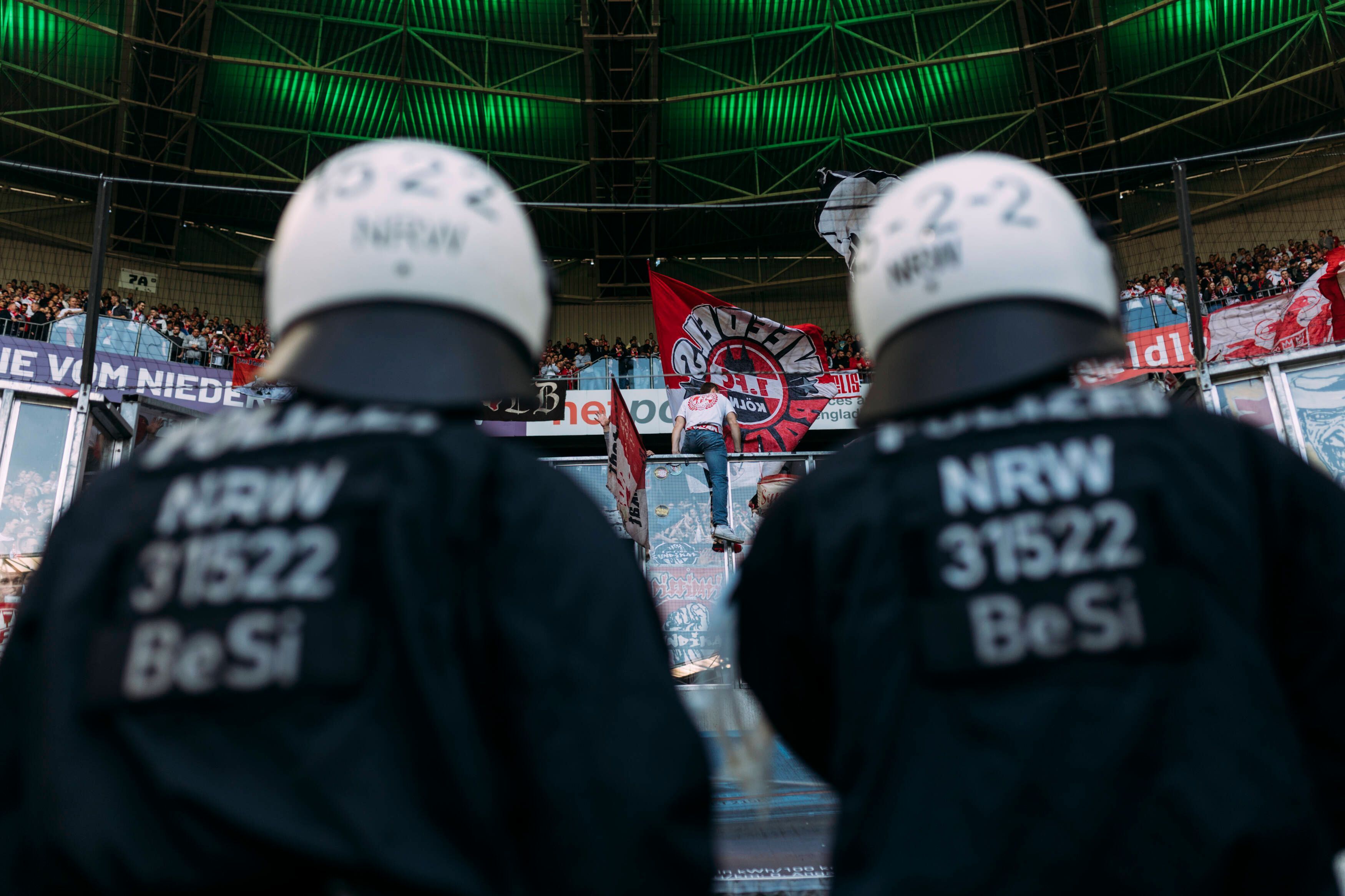 Polizeikräfte beobachten den Gästeblock im Borussia-Park. Dieses Symbol-Foto stammt vom Bundesliga-Derby zwischen Borussia Mönchengladbach und dem 1. FC Köln am 16. April 2022. Zu sehen sind zwei Polizisten in Einsatzmontur, sie tragen Schutzhelme und blicken hoch zu den FC-Fans.