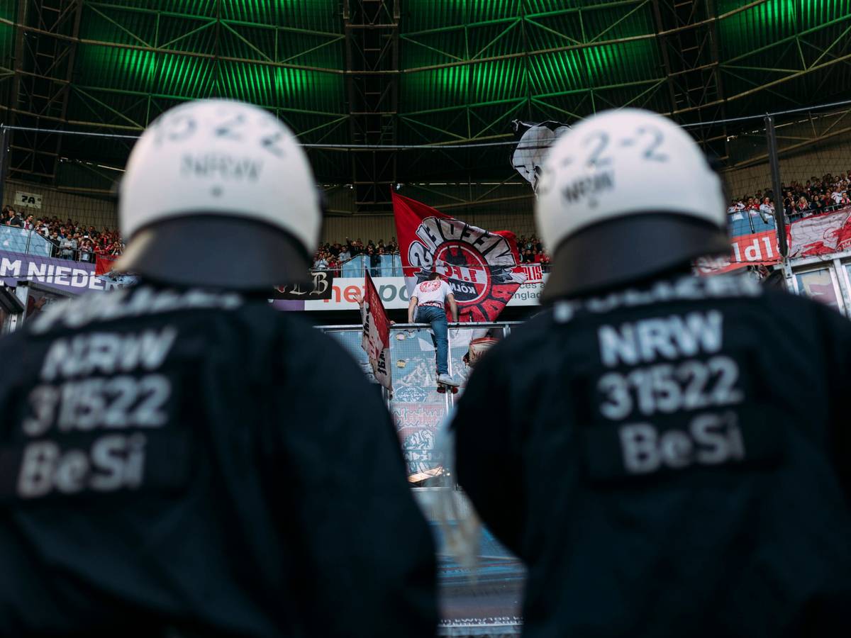 Polizeikräfte beobachten den Gästeblock im Borussia-Park. Dieses Symbol-Foto stammt vom Bundesliga-Derby zwischen Borussia Mönchengladbach und dem 1. FC Köln am 16. April 2022. Zu sehen sind zwei Polizisten in Einsatzmontur, sie tragen Schutzhelme und blicken hoch zu den FC-Fans.