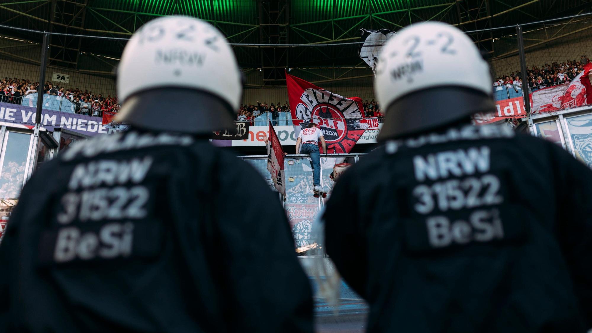 Polizeikräfte beobachten den Gästeblock im Borussia-Park. Dieses Symbol-Foto stammt vom Bundesliga-Derby zwischen Borussia Mönchengladbach und dem 1. FC Köln am 16. April 2022. Zu sehen sind zwei Polizisten in Einsatzmontur, sie tragen Schutzhelme und blicken hoch zu den FC-Fans.