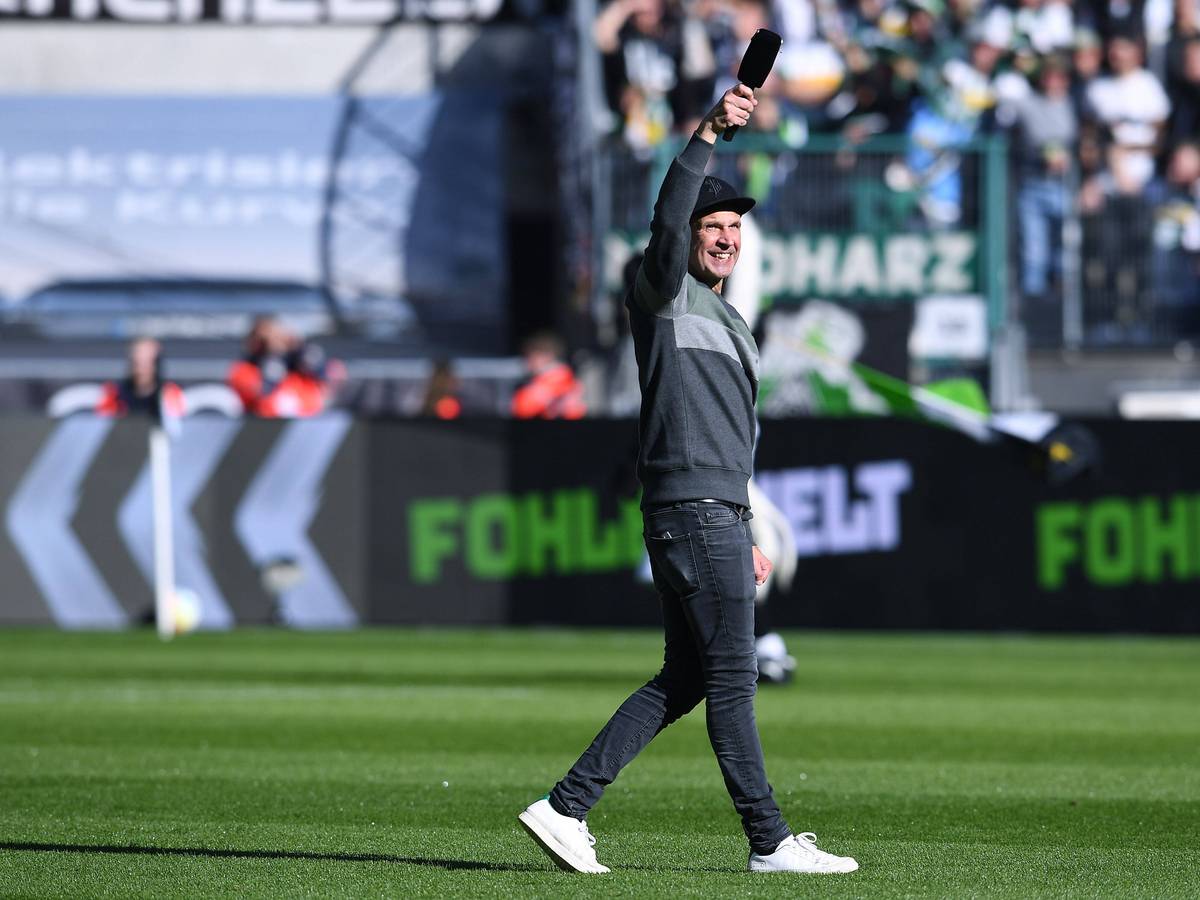 Stadionsprecher Torsten „Knippi“ Knippertz am 9. Oktober 2022 vor dem Bundesliga-Heimspiel von Borussia Mönchengladbach gegen den 1. FC Köln. Knippertz steht auf dem Rasen im Borussia-Park, in der rechten Hand hält er ein Mikrofon.