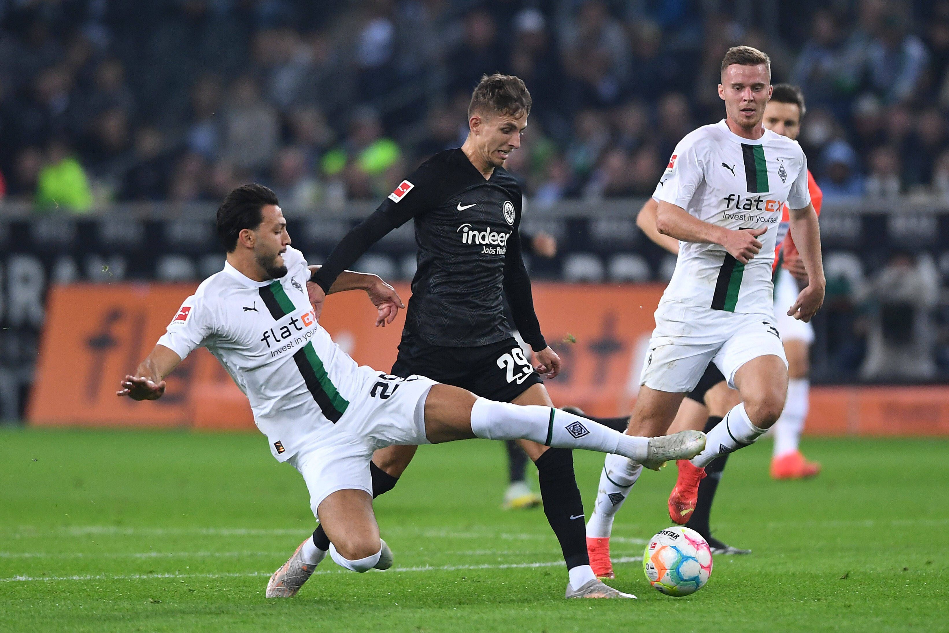 Ramy Bensebaini (l.) und Nico Elvedi (r.) von Borussia Mönchengladbach am 22. Oktober 2022 im Zweikampf mit Jesper Lindström von Eintracht Frankfurt. Bensebaini grätscht zum Ball.