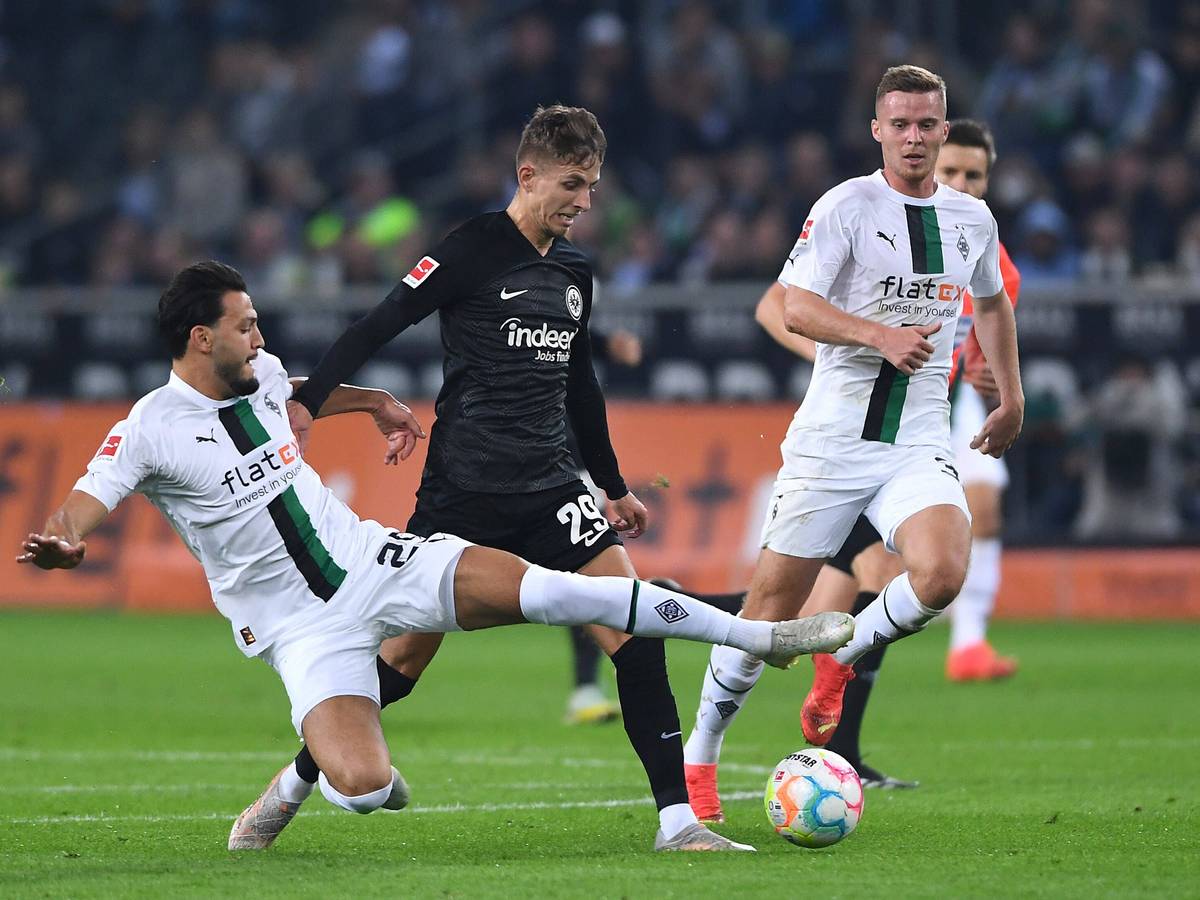 Ramy Bensebaini (l.) und Nico Elvedi (r.) von Borussia Mönchengladbach am 22. Oktober 2022 im Zweikampf mit Jesper Lindström von Eintracht Frankfurt. Bensebaini grätscht zum Ball.
