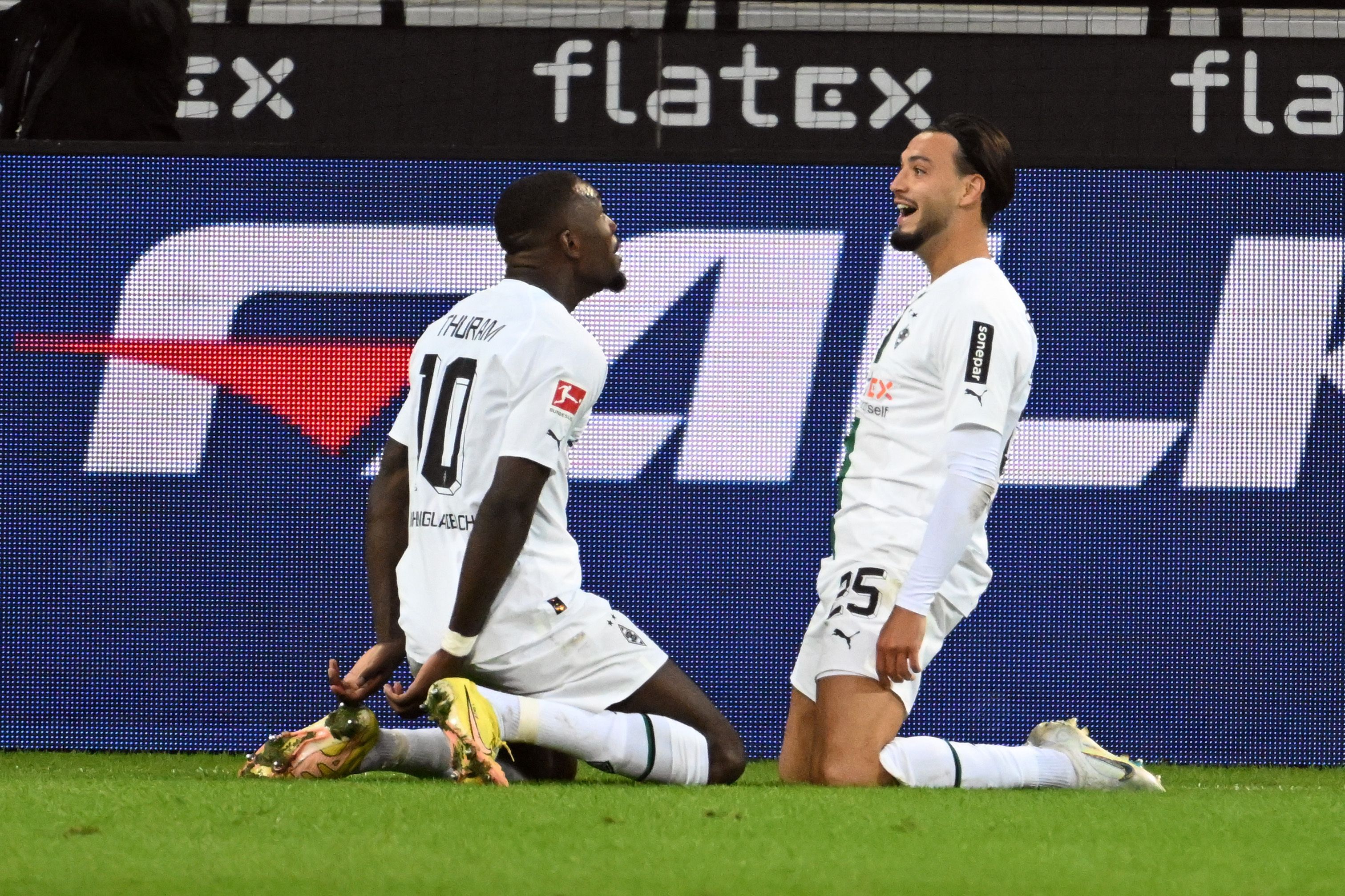 Die Gladbach-Stars Marcus Thuram (l.) und Ramy Bensebaini (r.) jubeln gemeinsam über einen Treffer im Borussia-Park, hier zu sehen am 17. September 2022 beim Bundesliga-Duell gegen RB Leipzig. Die beiden knien auf dem Rasen.