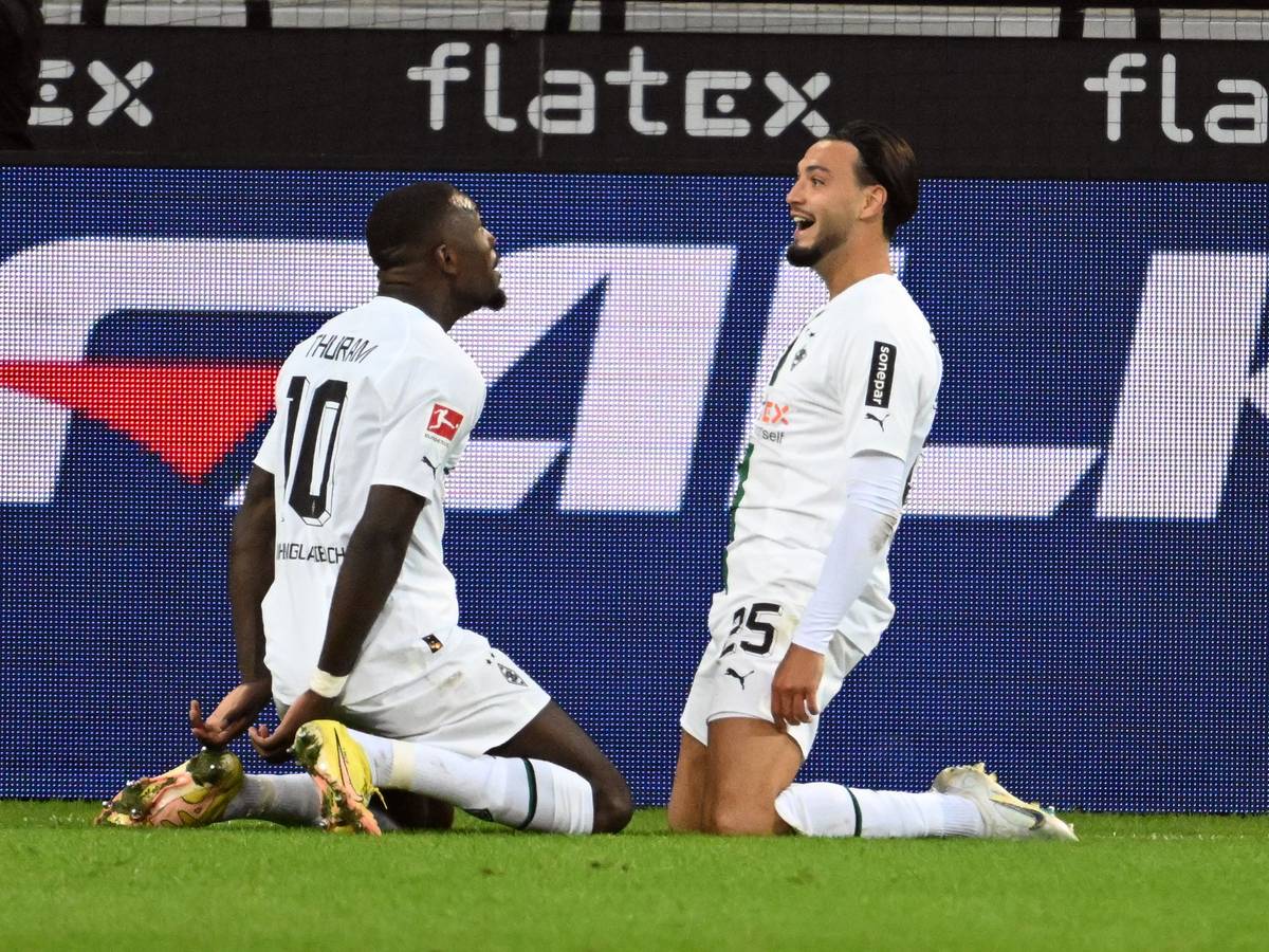 Die Gladbach-Stars Marcus Thuram (l.) und Ramy Bensebaini (r.) jubeln gemeinsam über einen Treffer im Borussia-Park, hier zu sehen am 17. September 2022 beim Bundesliga-Duell gegen RB Leipzig. Die beiden knien auf dem Rasen.