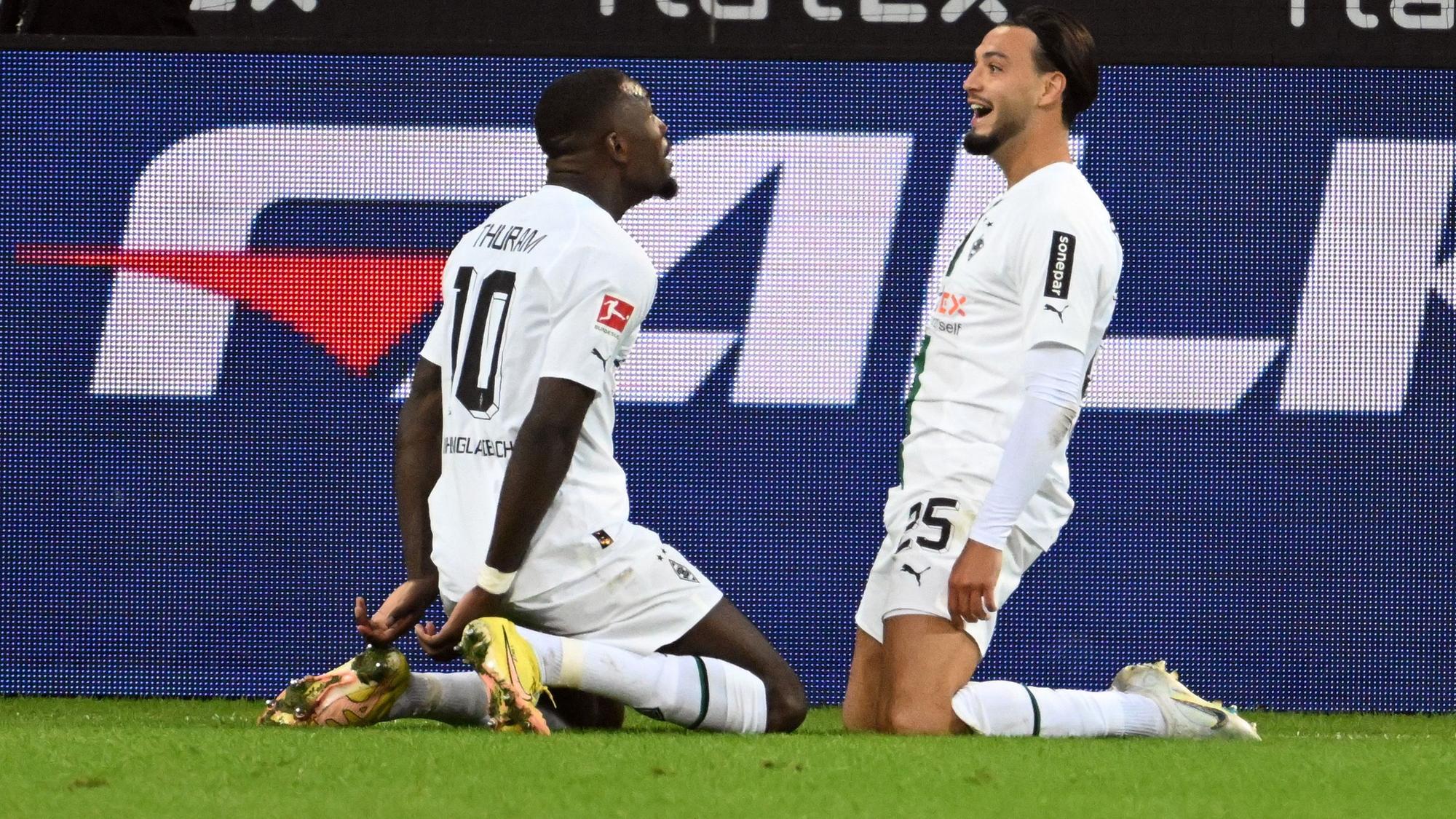 Die Gladbach-Stars Marcus Thuram (l.) und Ramy Bensebaini (r.) jubeln gemeinsam über einen Treffer im Borussia-Park, hier zu sehen am 17. September 2022 beim Bundesliga-Duell gegen RB Leipzig. Die beiden knien auf dem Rasen.