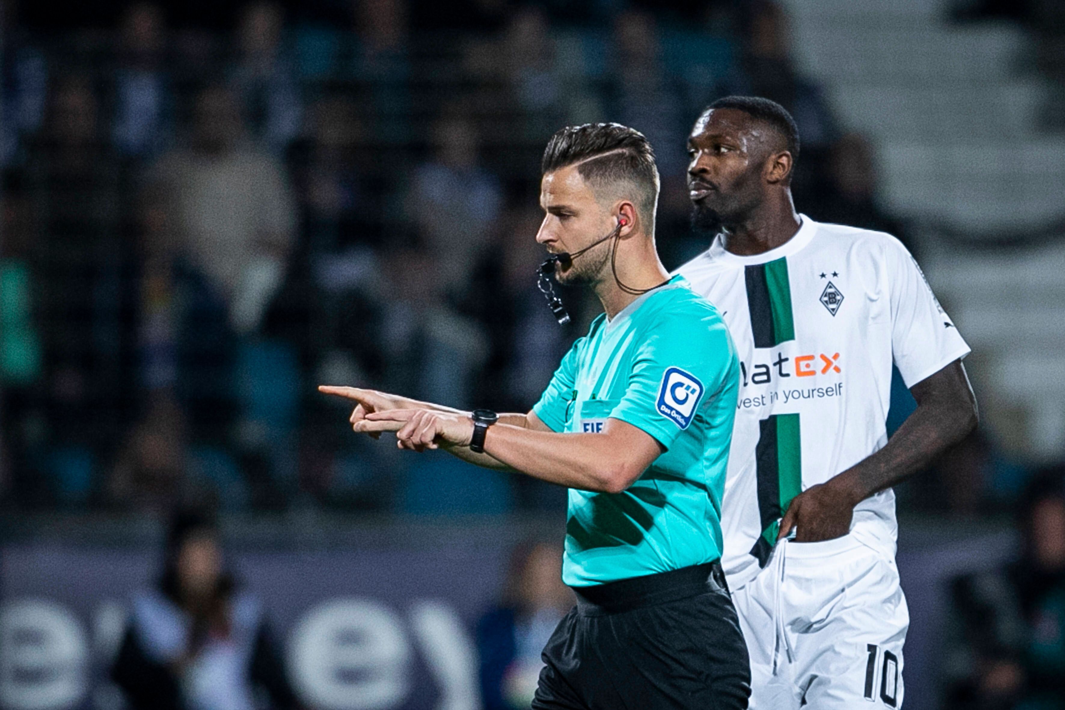 Schiedsrichter Daniel Schlager zeigt an, dass es eine VAR-Entscheidung im Spiel VfL Bochum gegen Borussia Mönchengladbach am 8. November 2022 gibt. Borussia-Spieler Marcus Thuram steht dabei hinter ihm.