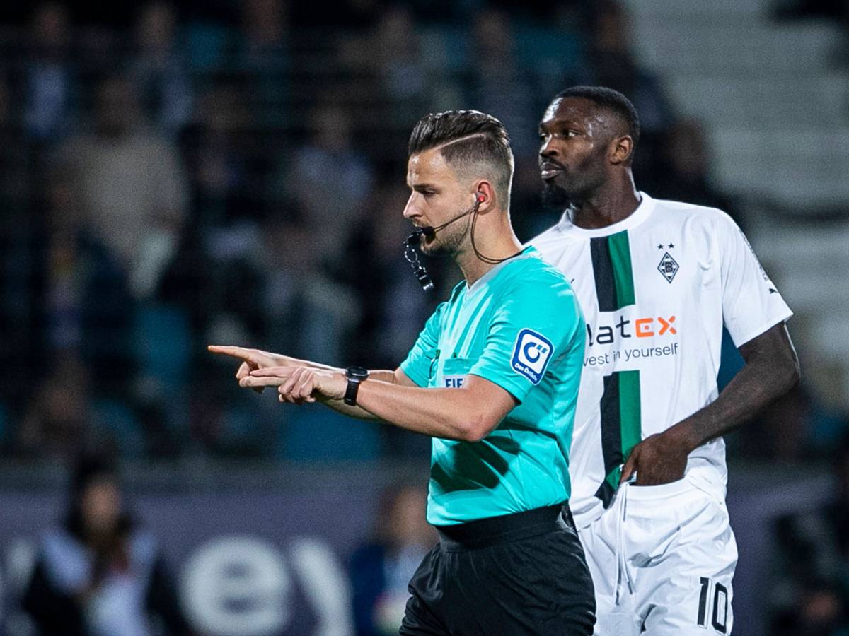 Schiedsrichter Daniel Schlager zeigt an, dass es eine VAR-Entscheidung im Spiel VfL Bochum gegen Borussia Mönchengladbach am 8. November 2022 gibt. Borussia-Spieler Marcus Thuram steht dabei hinter ihm.