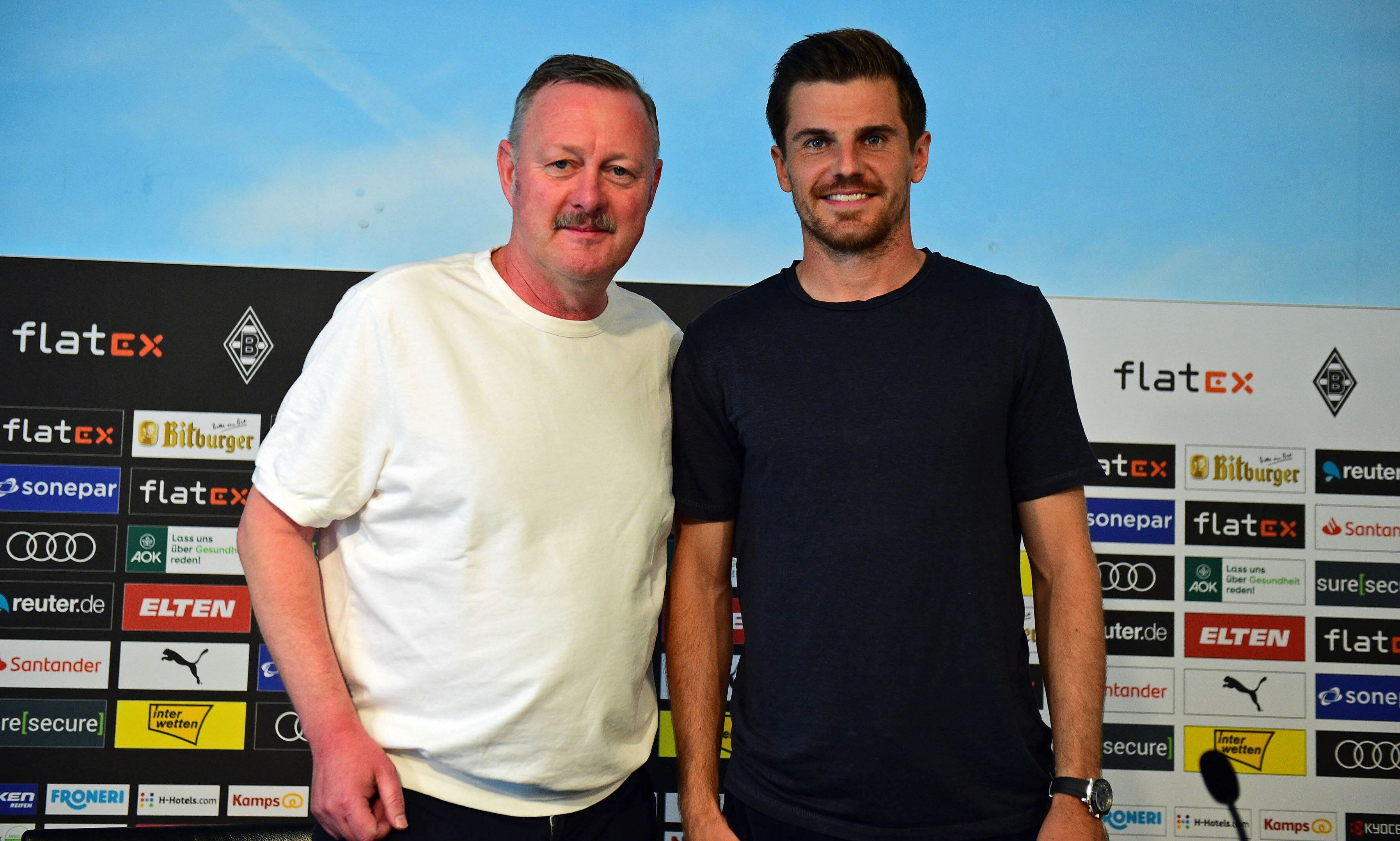 Gladbach-Manager Roland Virkus (l.) ist stolz auf seinen DFB-Nationalspieler Jonas Hofmann (r.), der am Donnerstag (10. November 2022) von Bundestrainer Hansi Flick für die WM in Katar nominiert worden ist. Auf diesem Foto sind die beiden am 9. August im Borussia-Park zu sehen. Virkus und Hofmann lächeln und schauen in die Kamera des Fotografen.