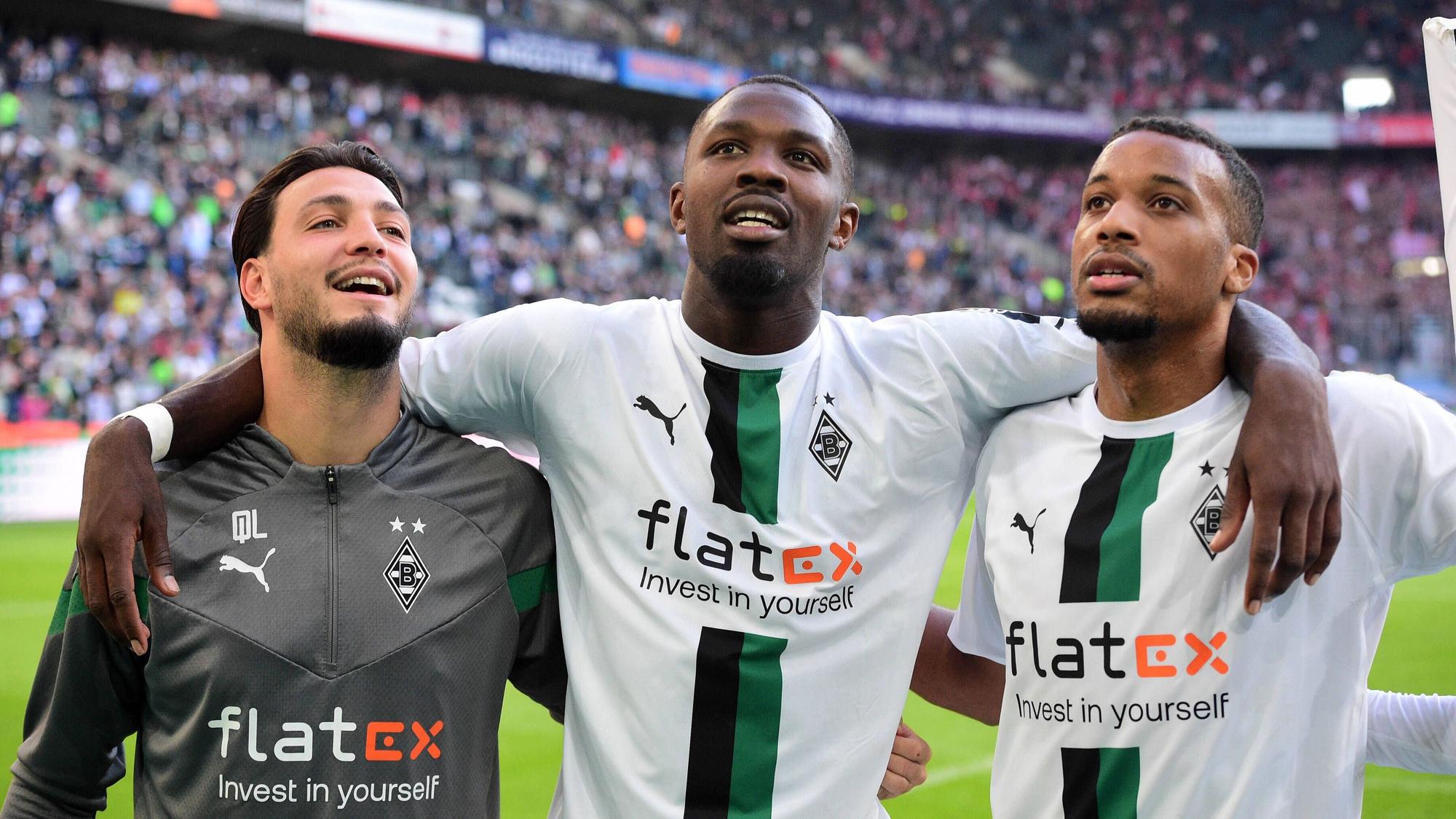 Die Gladbach-Profis Alassane Plea, Marcus Thuram und Ramy Bensebaini (v.r.n.l.). Auf diesem Bild sind die Borussia-Stars nach dem Derby-Sieg gegen 1. FC Köln am 9. Oktober 2022 im Borussia-Park zu sehen. Die Spieler umarmen sich und lächeln derweil.