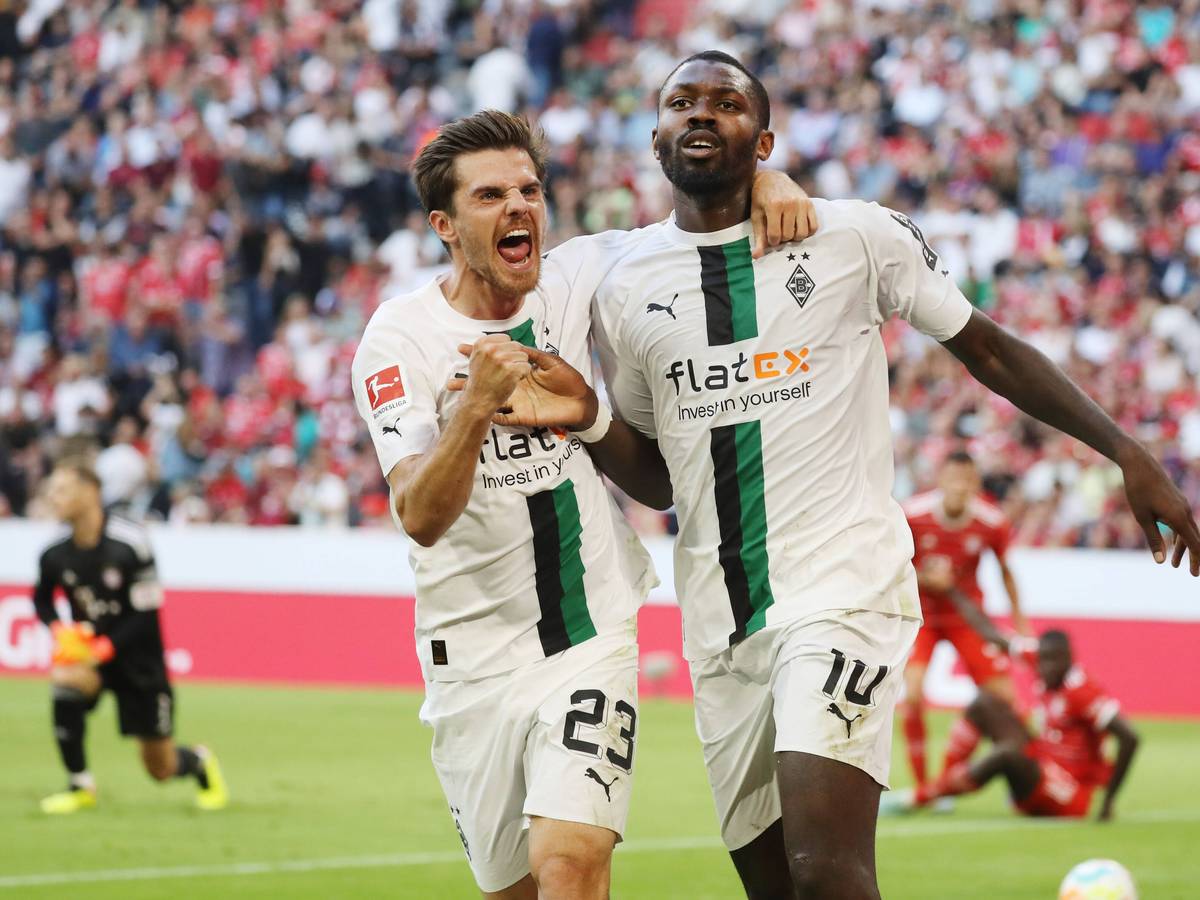Die Gladbach-Profis Marcus Thuram (r.) und Jonas Hofmann (l,) sind bei der Fußball-WM in Katar für ihr jeweiliges Land im Einsatz. Auf diesem Foto sind die beiden am 27. August 2022 in der Münchner Allianz-Arena zu sehen. Die beiden umarmen sich und jubeln.