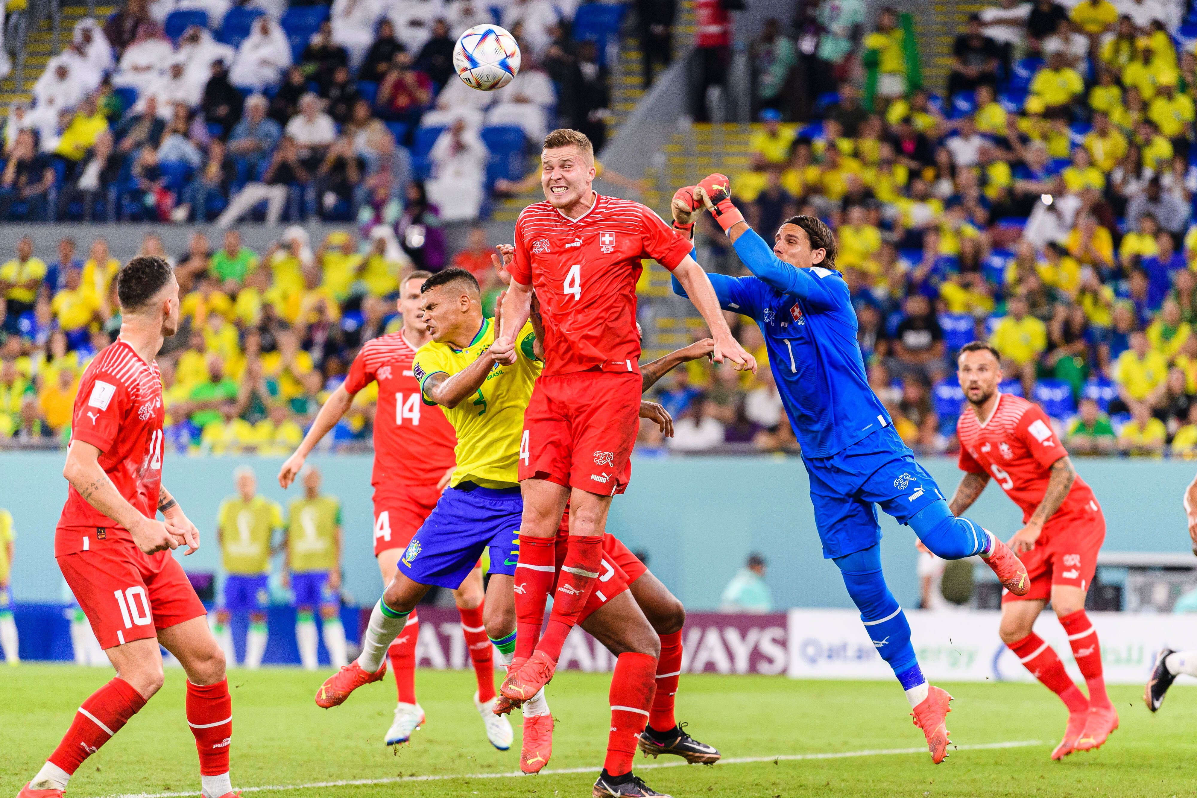Nico Elvedi von der Schweizer Nationalmannschaft springt hoch, um einen Ball gegen Brasilien wegzuköpfen. Yann Sommer springt dem Ball mit beiden Fäusten entgegen.
