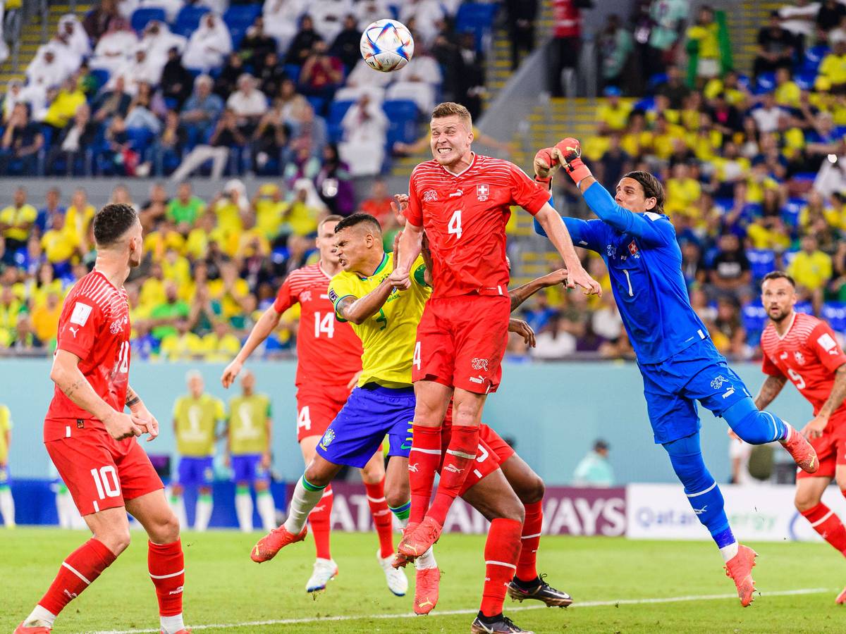 Nico Elvedi von der Schweizer Nationalmannschaft springt hoch, um einen Ball gegen Brasilien wegzuköpfen. Yann Sommer springt dem Ball mit beiden Fäusten entgegen.
