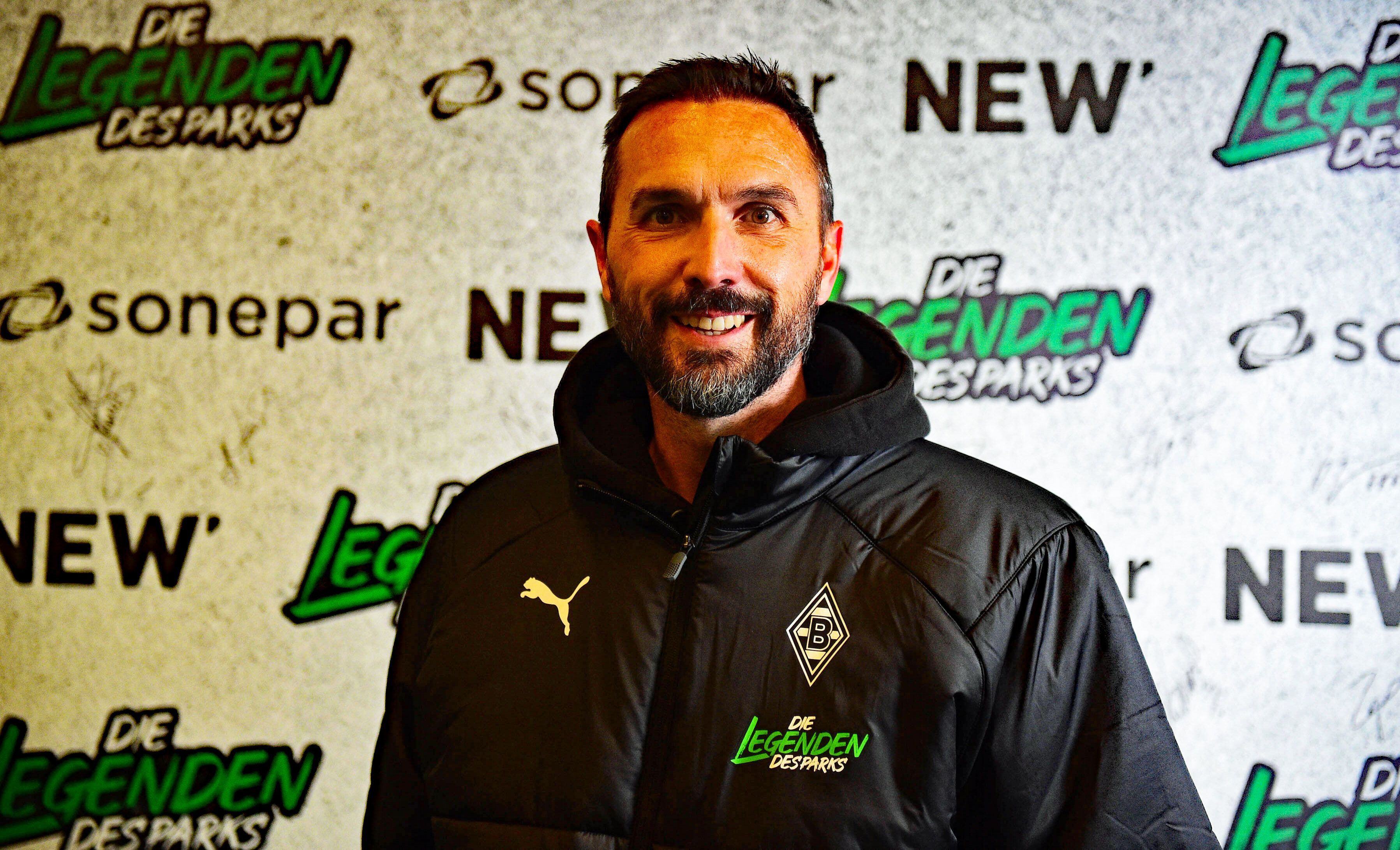 Ex-Gladbach-Kapitän Martin Stranzl, auf diesem Foto am 17. Dezember 2022, vor dem Legendenspiel im Borussia-Park, zu sehen. Stranzl steht vor einer Werbe-Tafel, er lächelt in die Kamera.