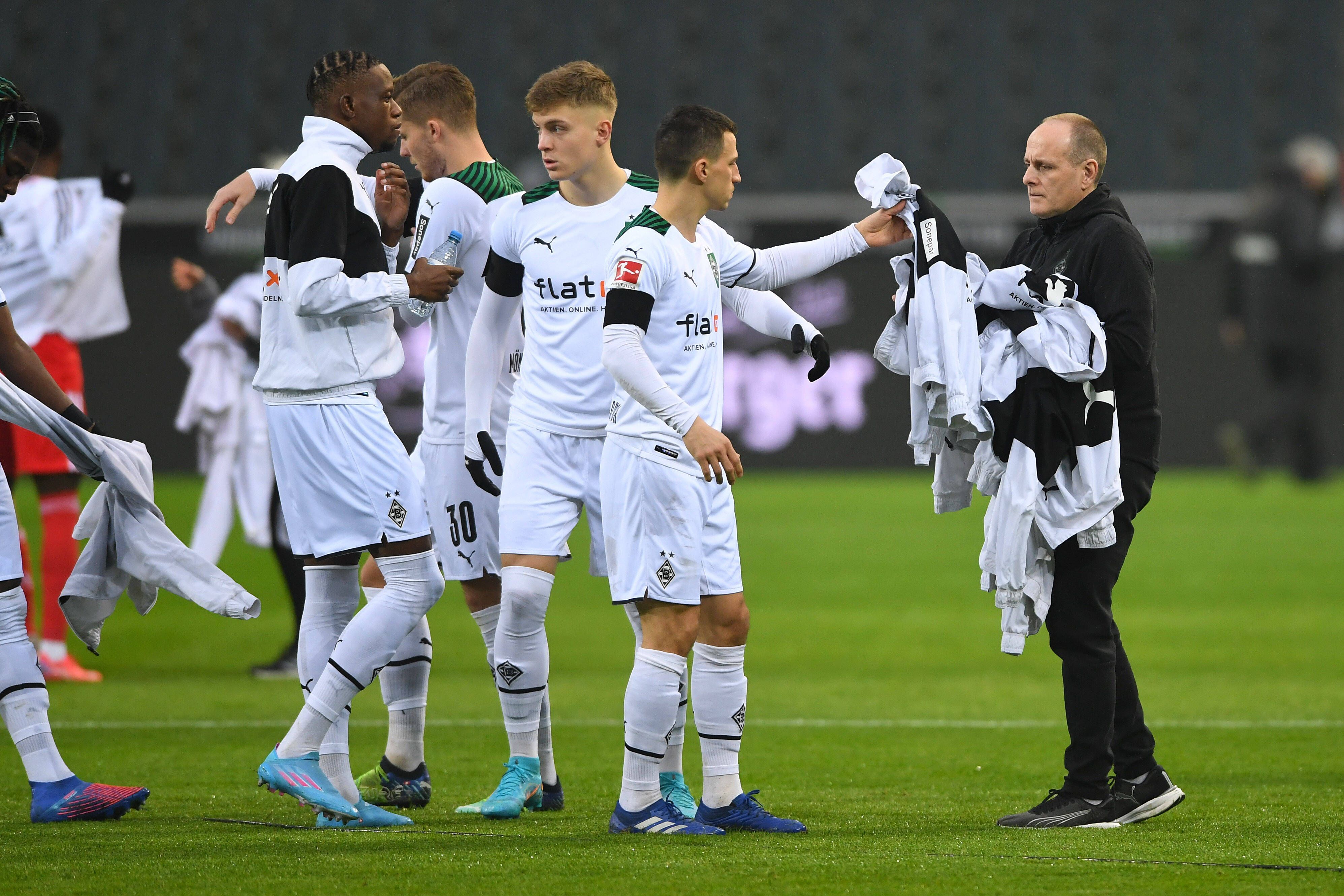 Marcus Breuer, Zeugwart bei Borussia Mönchengladbach, sammelt am 22. Januar 2022 weiße Jacken von Borussia-Profis vor dem Anpfiff ein. Stefan Lainer reicht dem Betreuer seine Jacke.