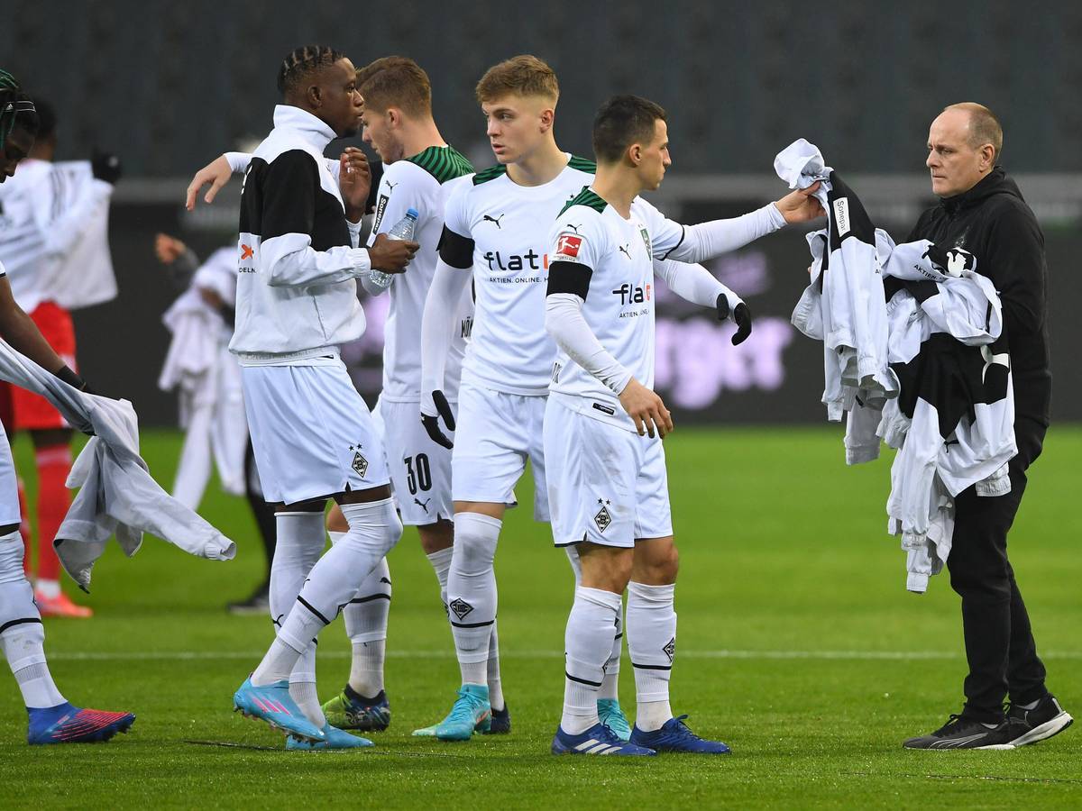 Marcus Breuer, Zeugwart bei Borussia Mönchengladbach, sammelt am 22. Januar 2022 weiße Jacken von Borussia-Profis vor dem Anpfiff ein. Stefan Lainer reicht dem Betreuer seine Jacke.