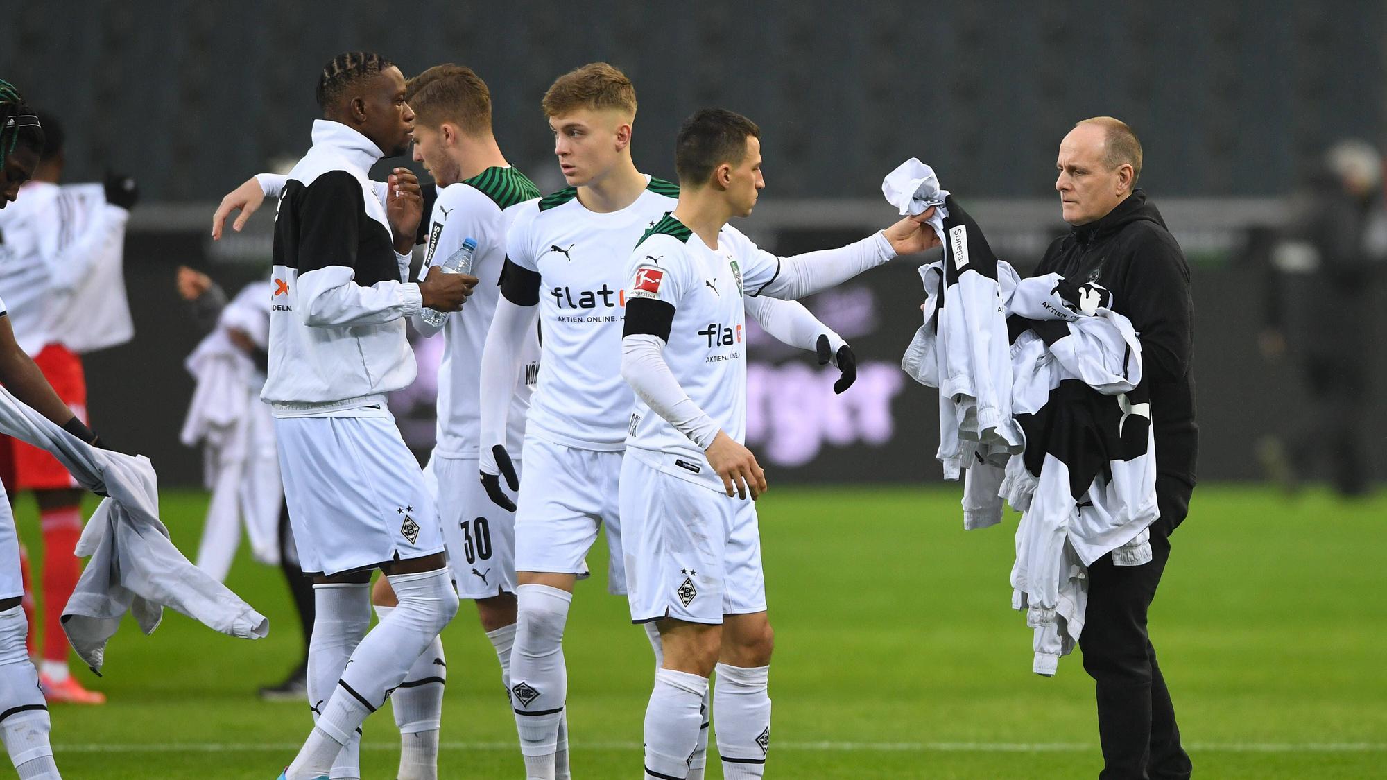 Marcus Breuer, Zeugwart bei Borussia Mönchengladbach, sammelt am 22. Januar 2022 weiße Jacken von Borussia-Profis vor dem Anpfiff ein. Stefan Lainer reicht dem Betreuer seine Jacke.
