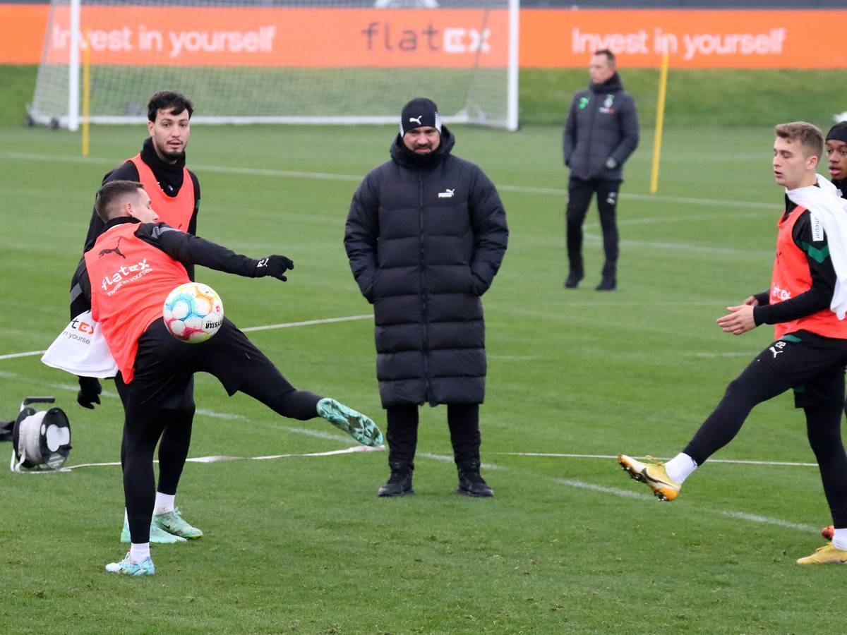 Trainings von Borussia Mönchengladbach im Borussia-Park am 22. Dezember 2022. Trainer Daniel Farke (M.) schaut seinen Spielern Conor Noß, Ramy Bensebaini, Oscar Fraulo und Yvandro Borges Sanches (v. l. n. r.) zu. Farke trägt eine lange Winterjacke und eine Mütze.