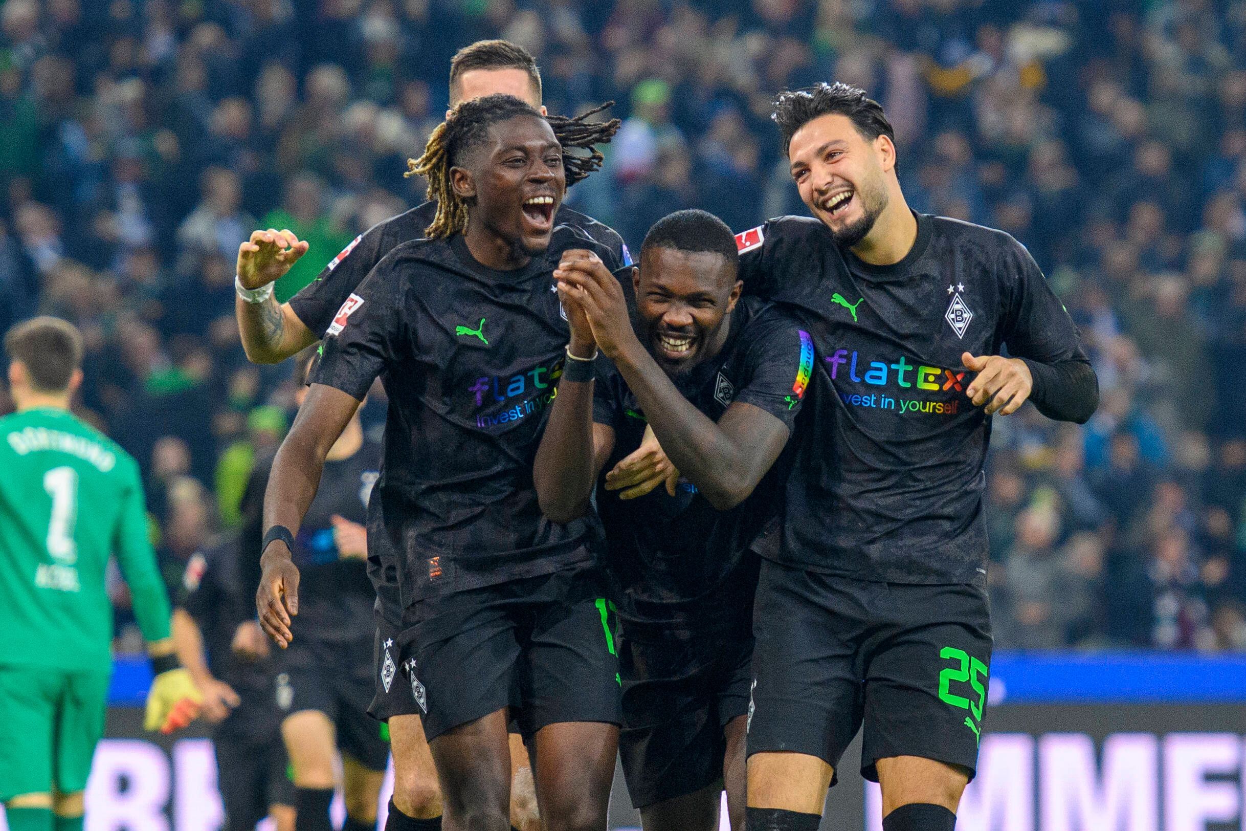 Manu Koné, Marcus Thuram und Ramy Bensebaini jubeln, lachen und liegen sich nach einem Tor im Bundesliga-Spiel gegen Borussia Dortmund am 11. November 2022 in den Armen. Die drei Gladbach-Spieler tragen schwarze Trikots und schwarze Hosen.