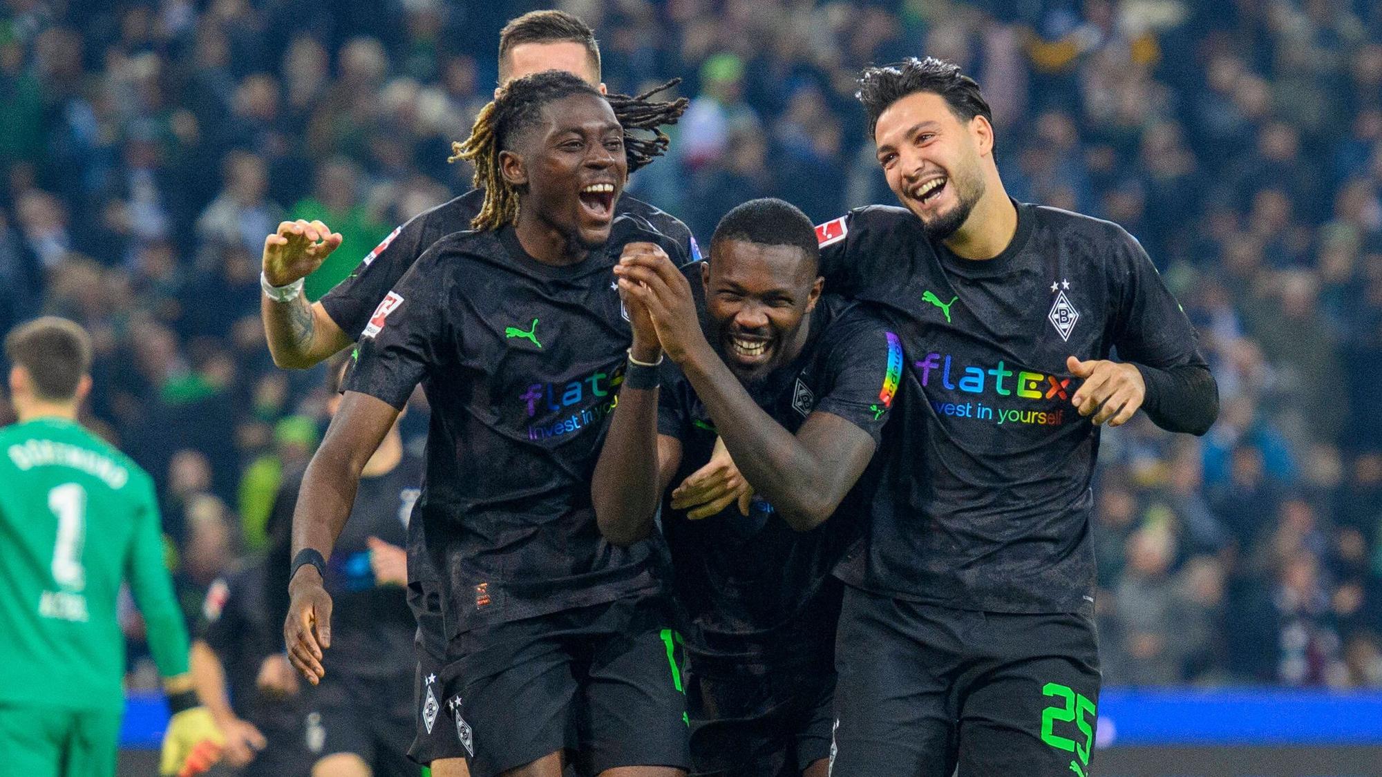 Manu Koné, Marcus Thuram und Ramy Bensebaini jubeln, lachen und liegen sich nach einem Tor im Bundesliga-Spiel gegen Borussia Dortmund am 11. November 2022 in den Armen. Die drei Gladbach-Spieler tragen schwarze Trikots und schwarze Hosen.