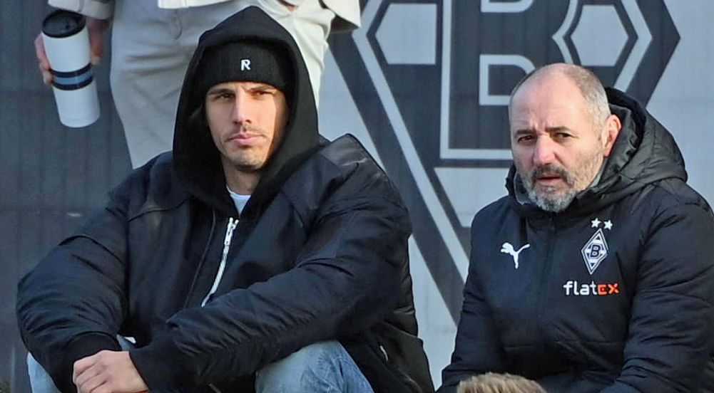 Gladbach-Torwart Yann Sommer (l.) sitzt am Samstag (7. Januar 2023) neben Co-Trainer Oliver Neuville (r.) und beobachtet das Testspiel seiner Team-Kollegen gegen Drittligist Oldenburg. Sommer hat eine Mütze auf.
