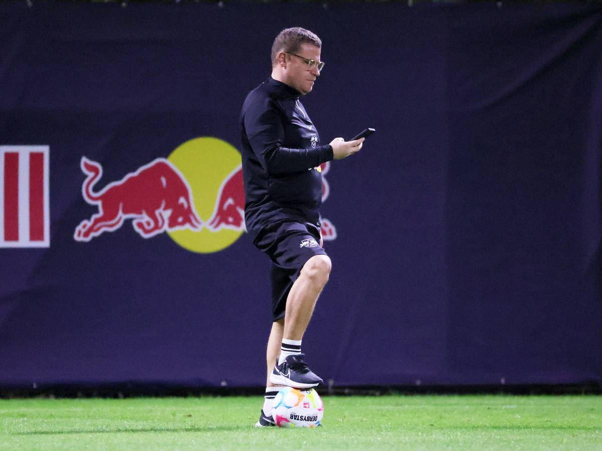 Ex-Gladbach-Manager Max Eberl ist mit seinem neuen Klub RB Leipzig im Trainingslager in Abu Dhabi. Auf diesem Foto ist der 49-Jährige am 3. Januar 2023 zu sehen. Eberl hält in der rechten Hand sein Smartphone, auf das er blickt. Sein rechter Fuß steht auf einem Ball.