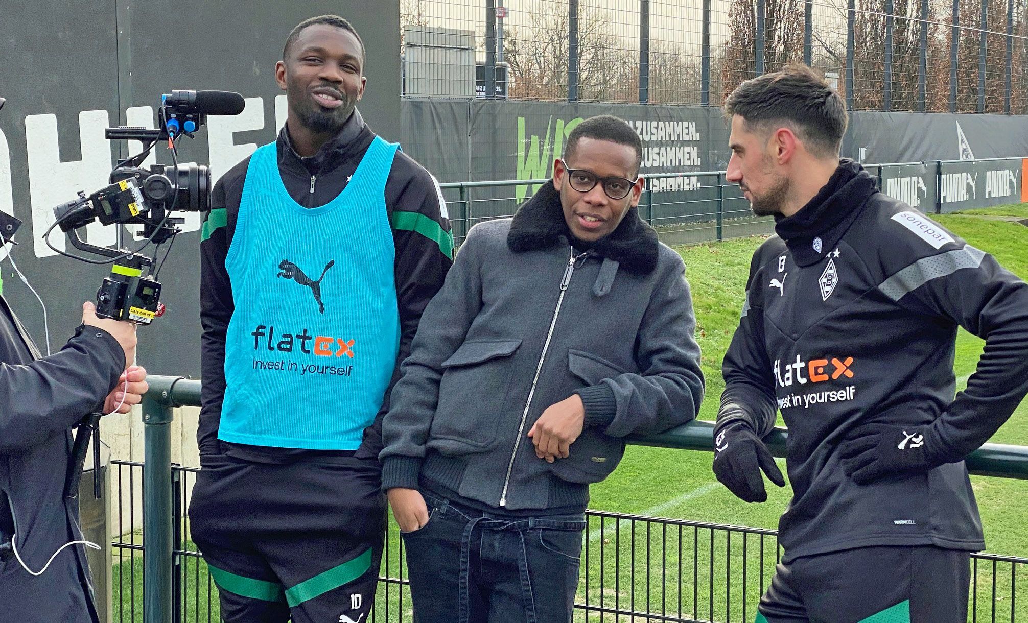 Ex-Gladbach-Star Ibrahima Traoré (M.), hier am Dienstag (10. Januar 2023) gemeinsam mit Marcus Thuram (l.) und Lars Stindl (r.) im Borussia-Park zu sehen, ist derzeit für einen französischen TV-Sender im Fohlen-Stall als Reporter unterwegs. Traoré spricht mit Stindl und Thuram, dabei werden die drei von einem Kameramann gefilmt.