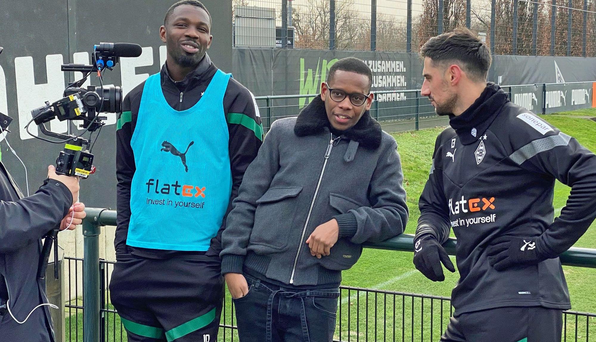 Ex-Gladbach-Star Ibrahima Traoré (M.), hier am Dienstag (10. Januar 2023) gemeinsam mit Marcus Thuram (l.) und Lars Stindl (r.) im Borussia-Park zu sehen, ist derzeit für einen französischen TV-Sender im Fohlen-Stall als Reporter unterwegs. Traoré spricht mit Stindl und Thuram, dabei werden die drei von einem Kameramann gefilmt.