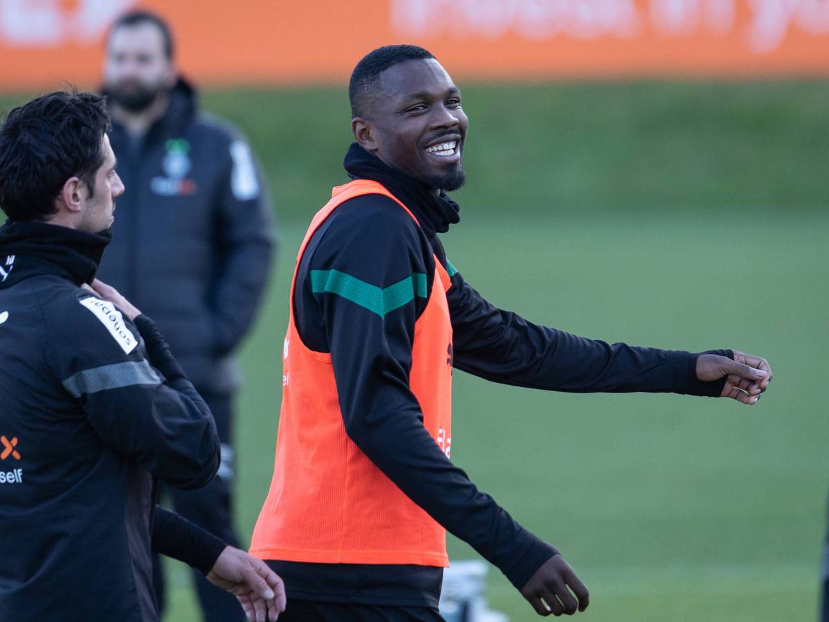 Marcus Thuram steht in Trainingskleidung und einem roten Leibchen am 6. Januar 2023 auf dem Trainingsplatz von Borussia Mönchengladbach. Der Fußballer lacht nach einem Gespräch mit Borussia-Teamkollege Lars Stindl.