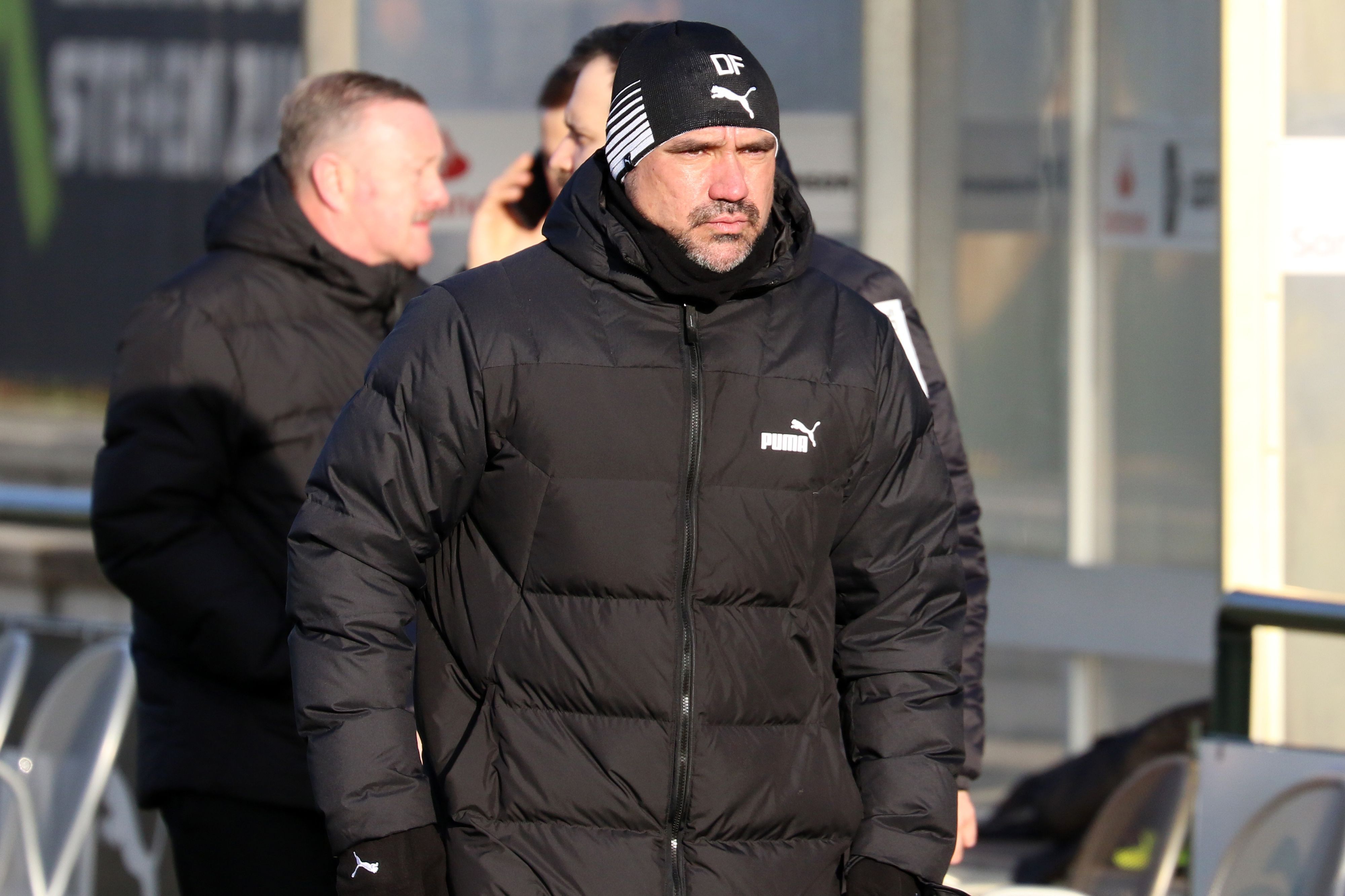 Daniel Farke, Trainer von Borussia Mönchengladbach, am 11. Januar 2023 beim Testspiel gegen Arminia Bielefeld (4:0) an der Seitenlinie. Er trägt eine dicke schwarze Winterjacke und eine schwarze Mütze mit seinen Initialen drauf und kneift die Augen von der Sonne geblendet zusammen.
